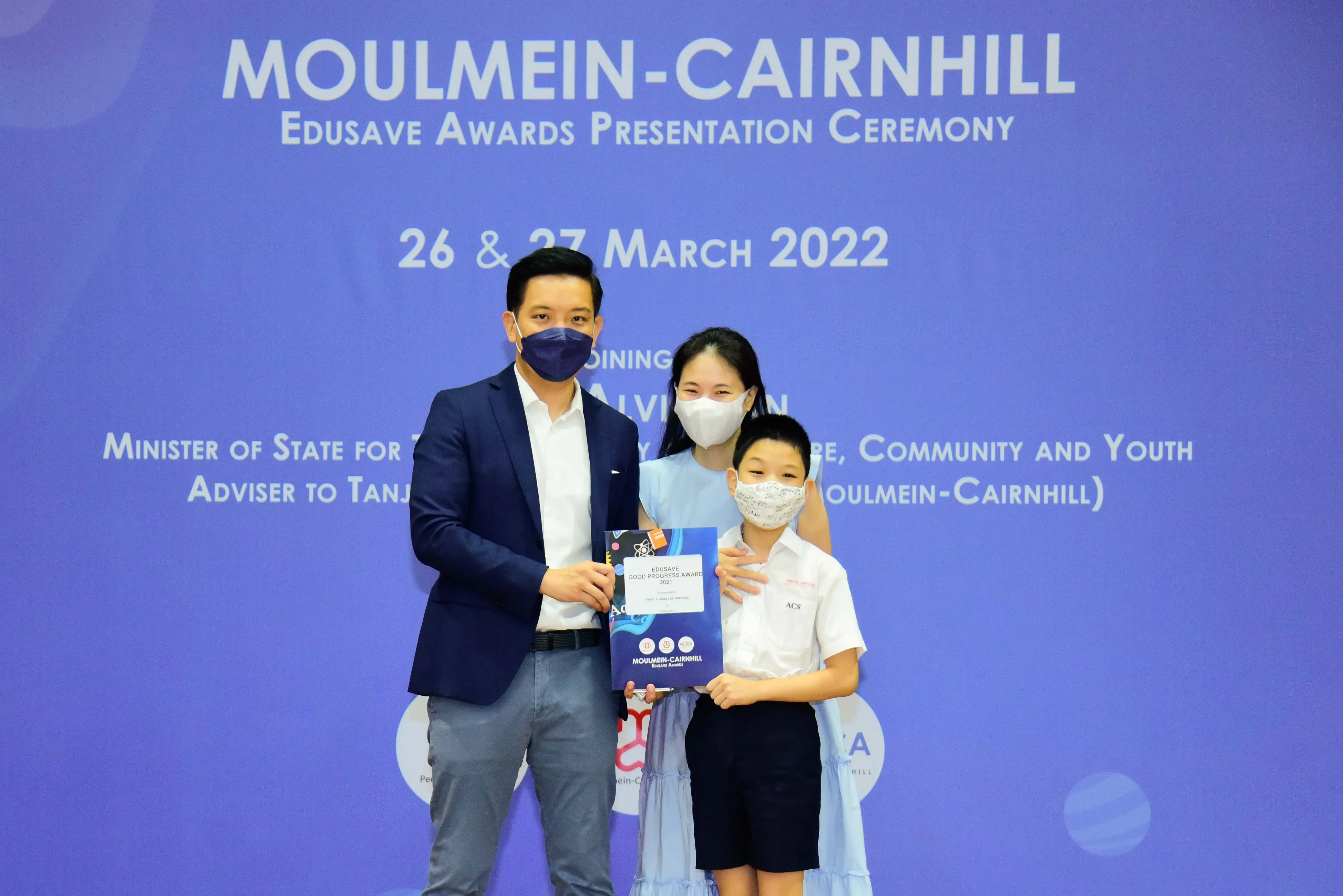 Three masked people pose with an award certificate at the Moulmein-Cairnhill Edusave Awards Ceremony, March 2022.
