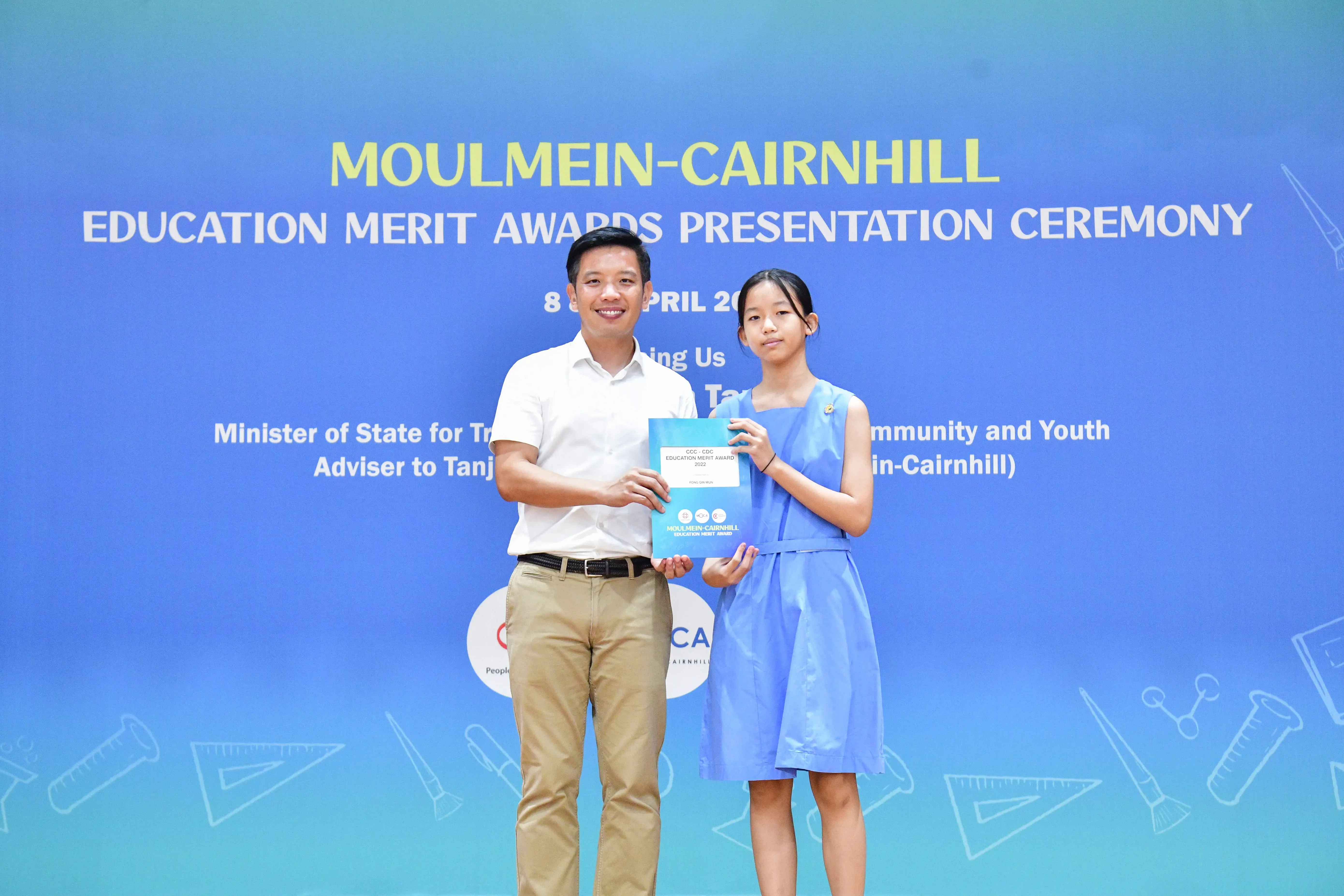 A man and a young girl hold an award certificate at the Moulmein-Cairnhill Education Merit Awards Presentation Ceremony.
