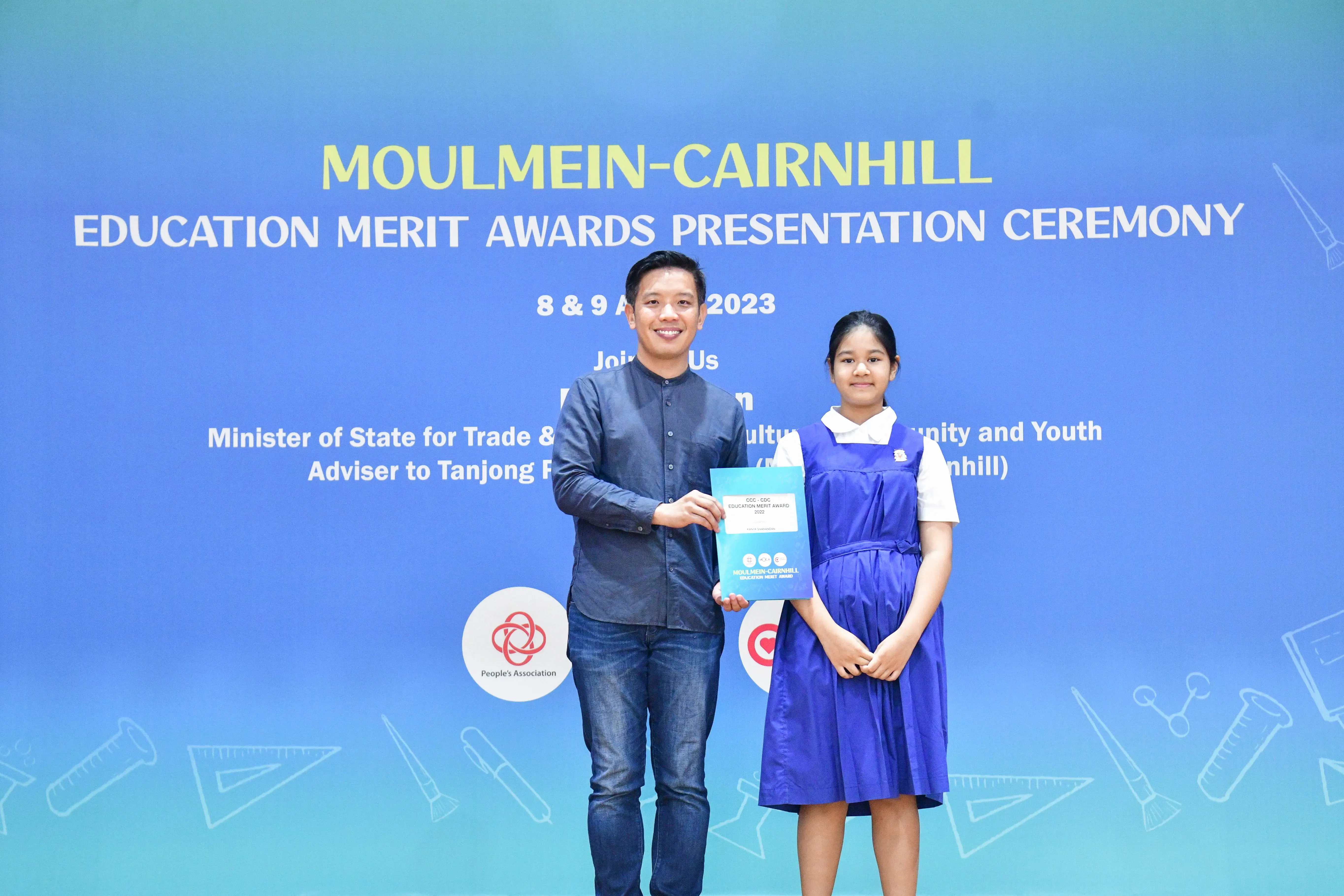 A man and a young girl in school uniform hold an award together at the Moulmein-Cairnhill Education Merit Awards 2023.