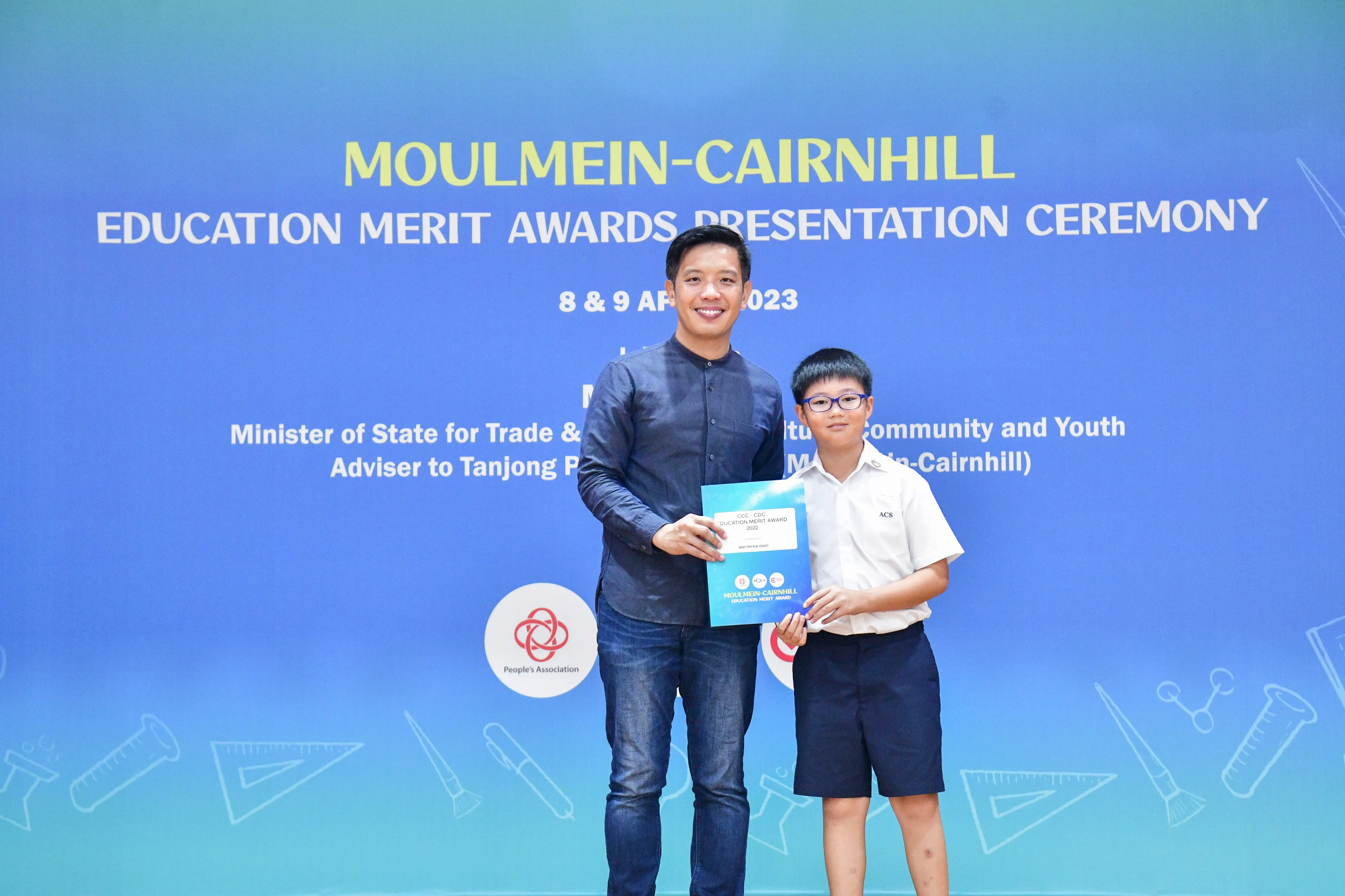 An adult and a young boy hold an award certificate at the Moulmein-Cairnhill Education Merit Awards Ceremony 2023.