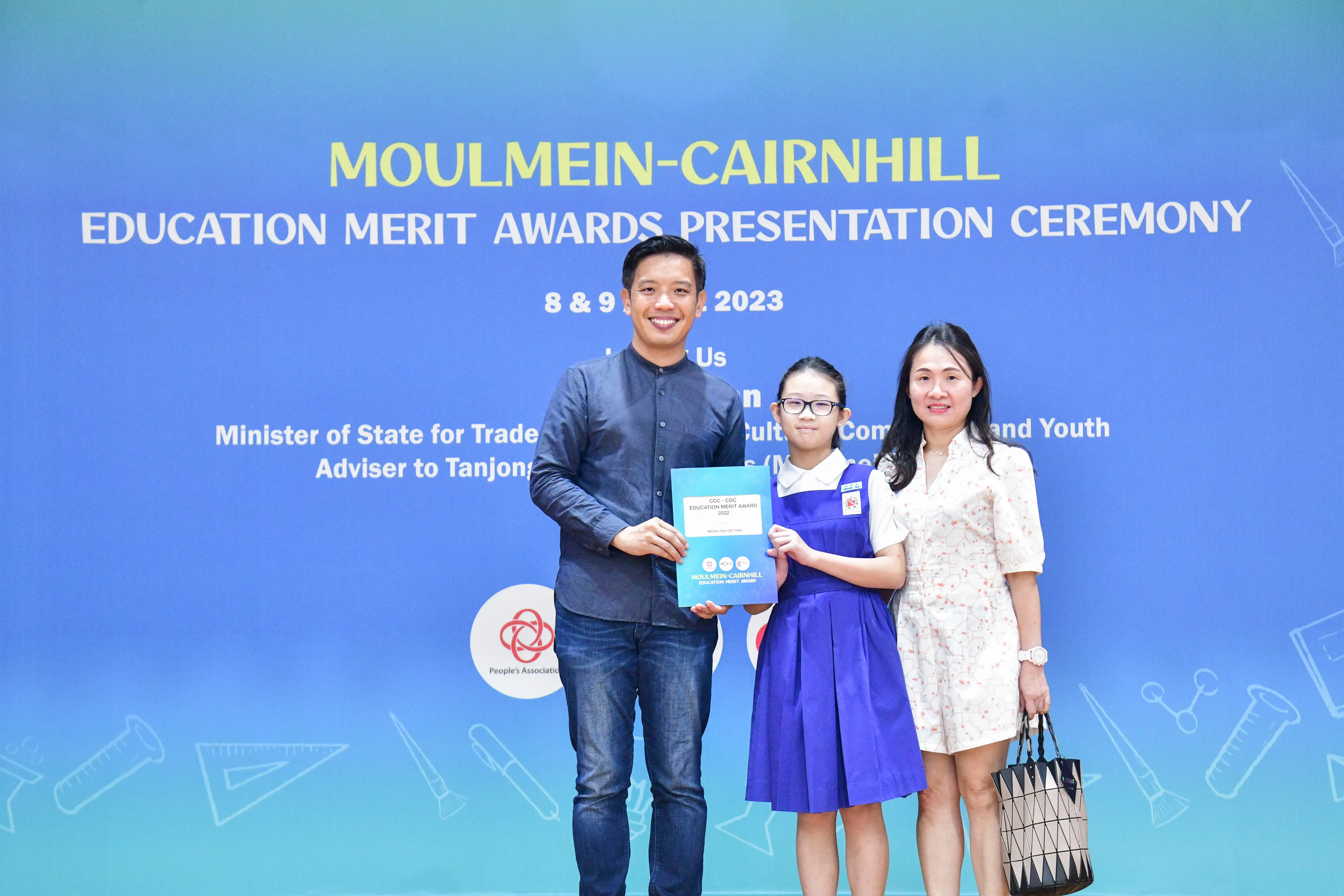 A man, young girl in school uniform, and woman pose holding a certificate at the Moulmein-Cairnhill Education Merit Awards 2023.