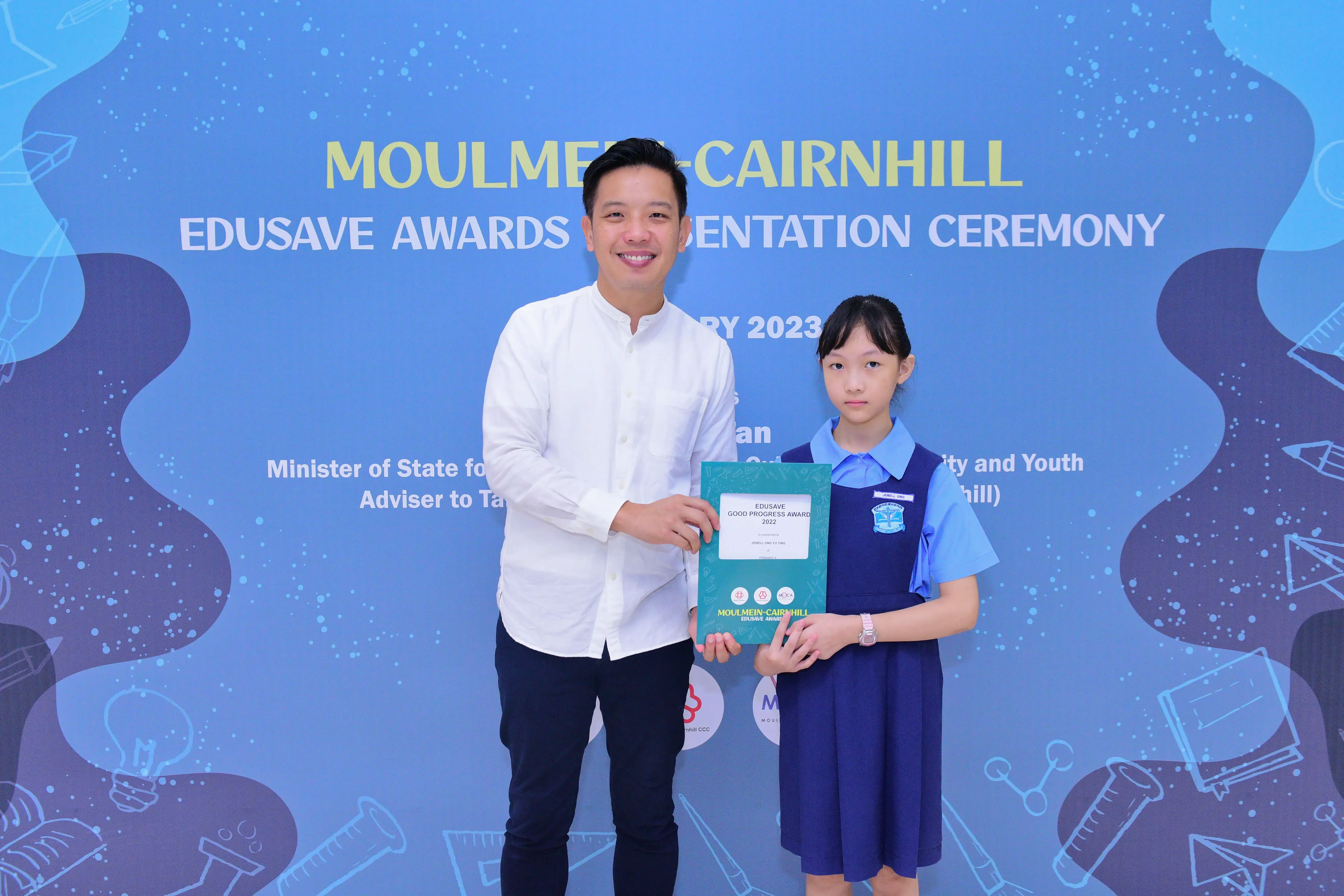 Man in white shirt and young girl in school uniform hold an award certificate at Moulmein-Cairnhill Edusave ceremony 2023.
