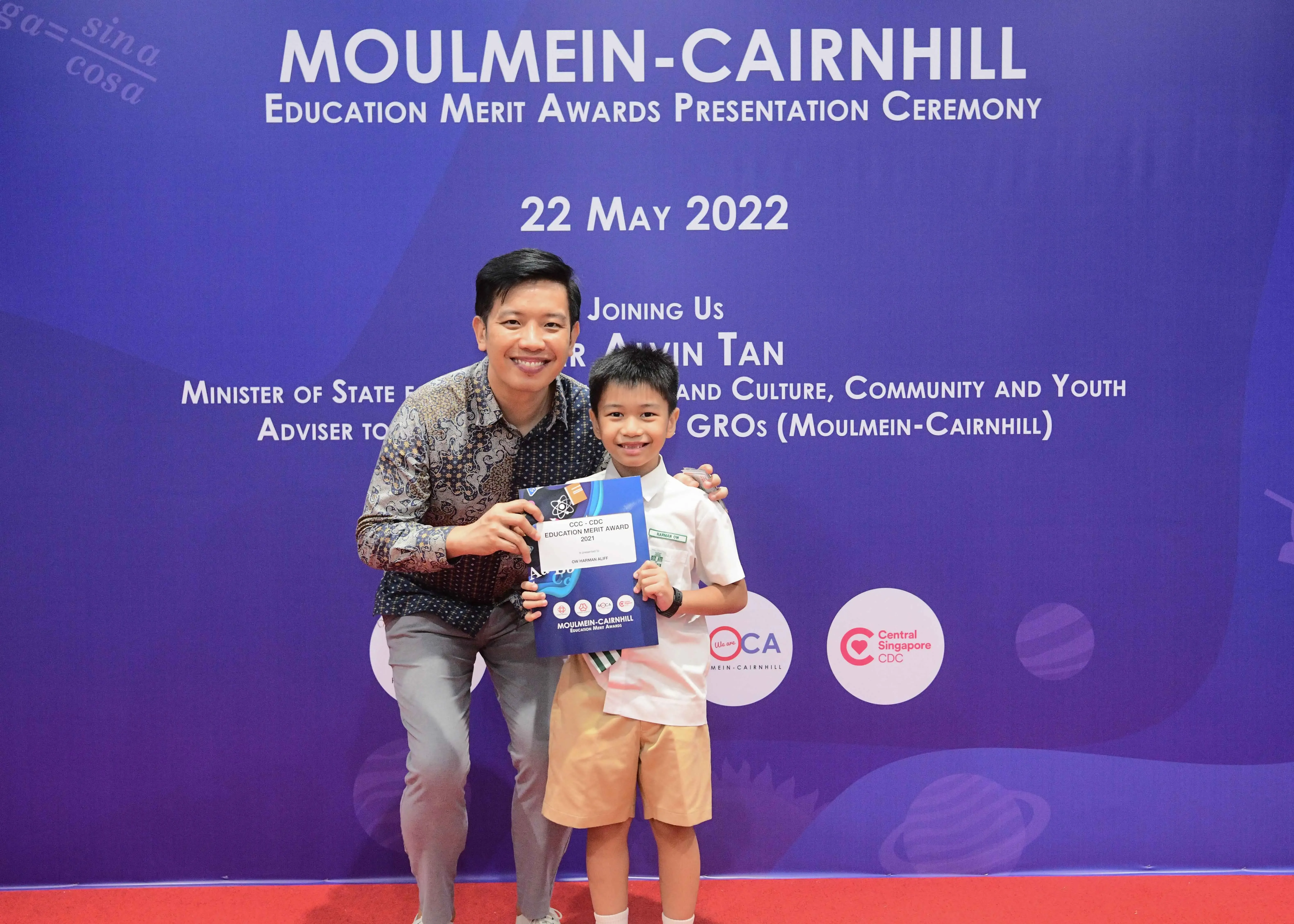 A man and a young boy hold an award certificate at the Moulmein-Cairnhill Education Merit Awards ceremony on 22 May 2022.