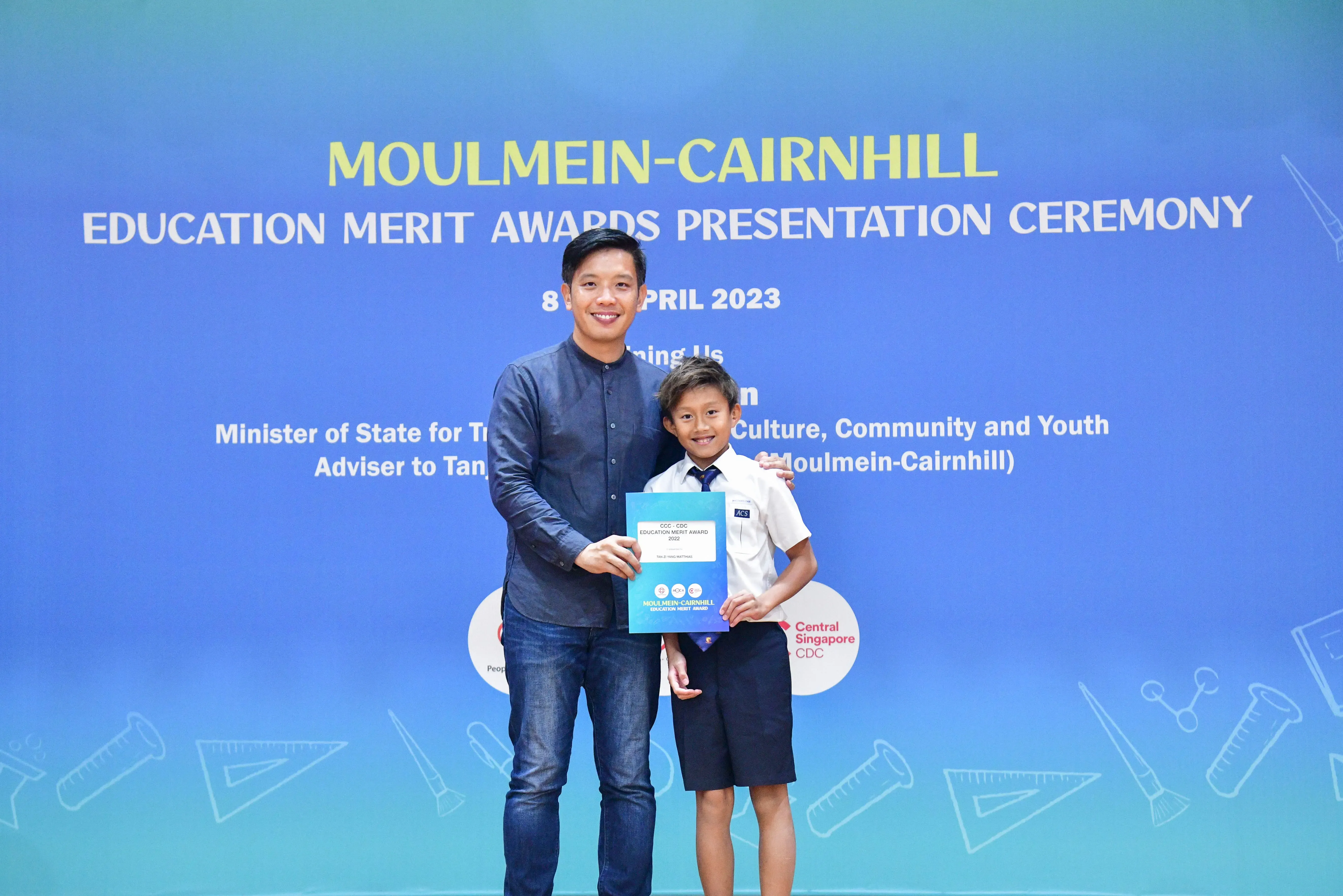 A man and a young boy hold a certificate at the Moulmein-Cairnhill Education Merit Awards Ceremony, April 2023.