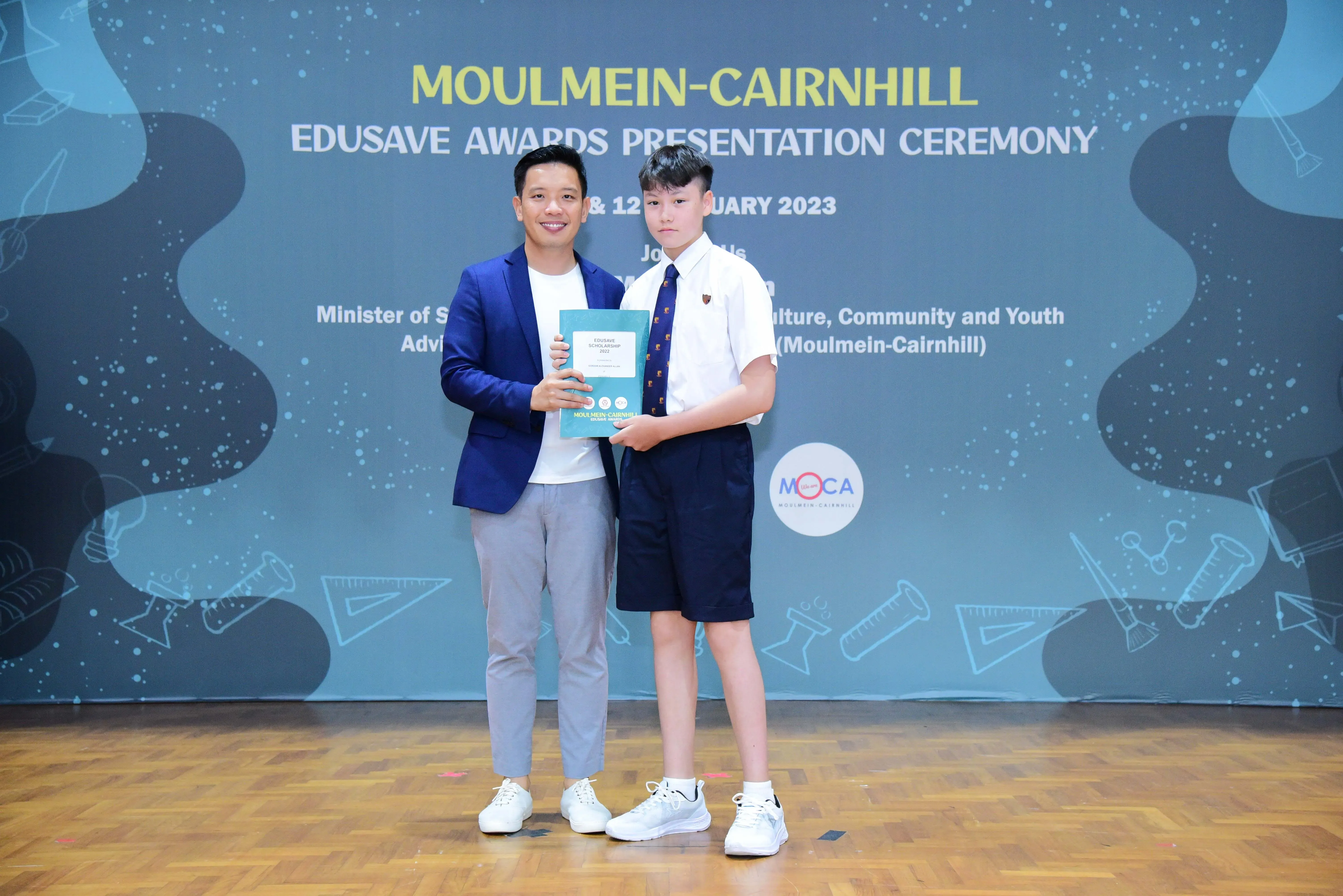 A man in a blue blazer and a student in school uniform hold a certificate at the Moulmein-Cairnhill Edusave Awards 2023.