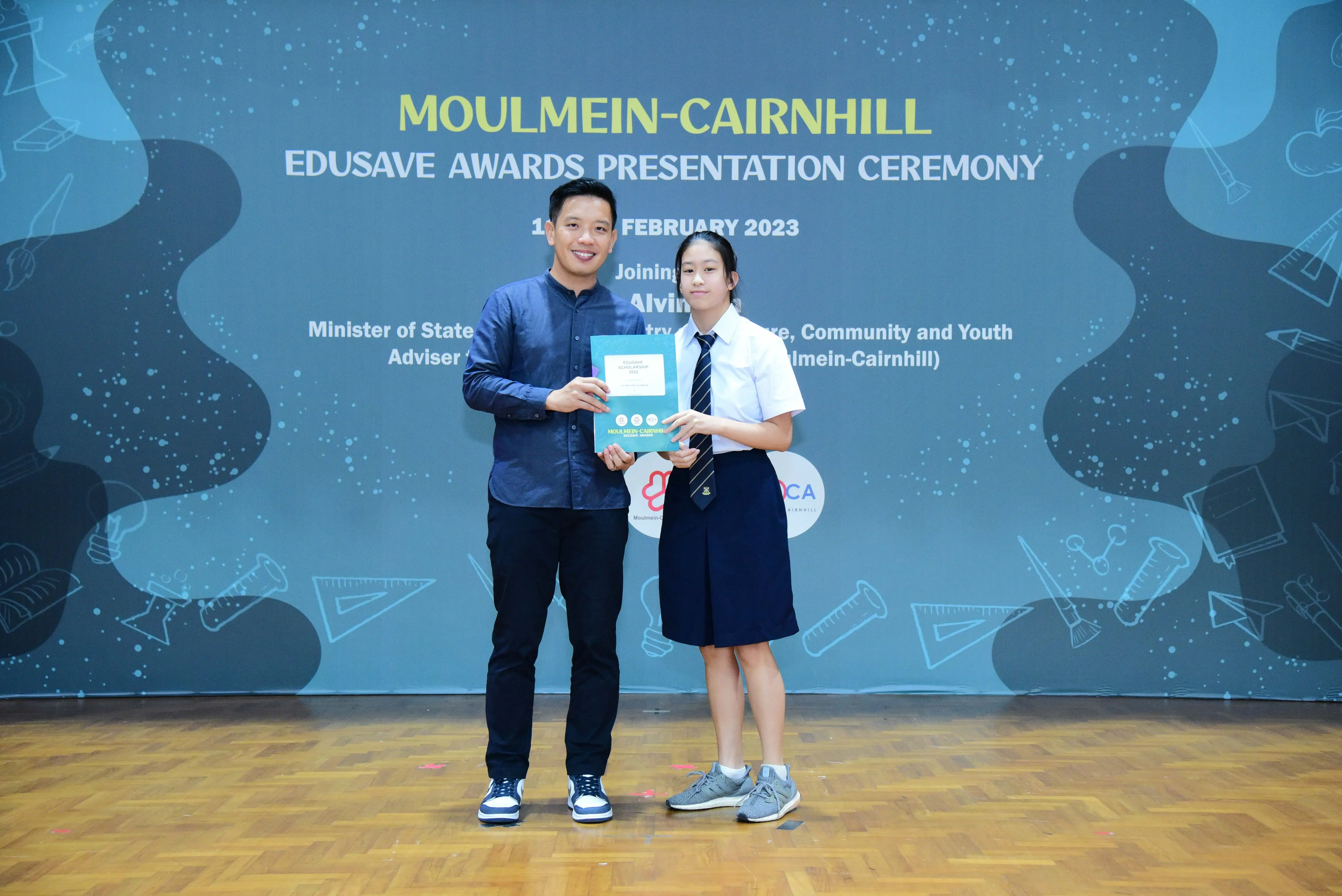 Two people hold an award certificate at the Moulmein-Cairnhill Edusave Awards Presentation Ceremony, February 2023.