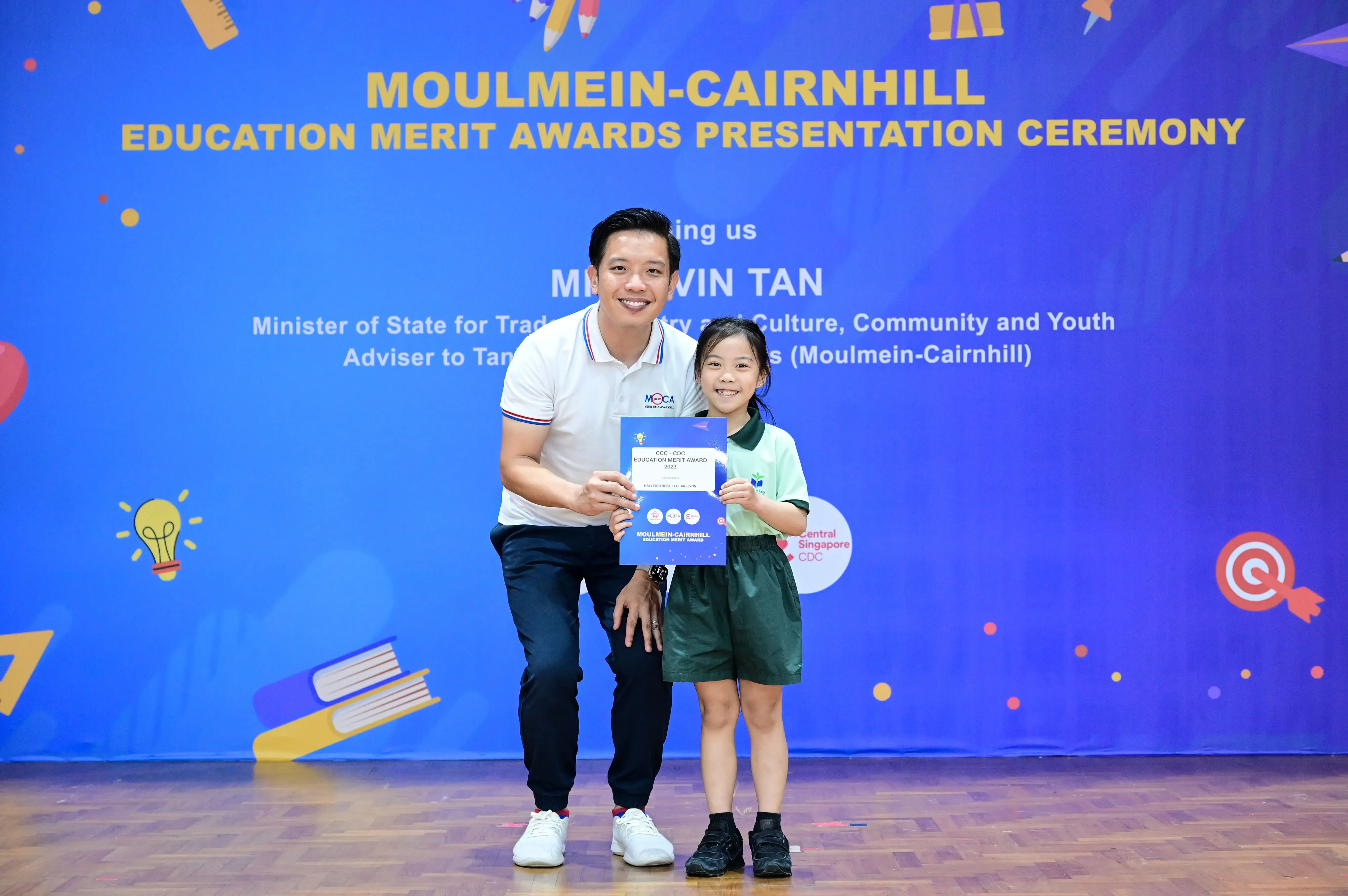 A man and a young girl hold a certificate at the Moulmein-Cairnhill Education Merit Awards Presentation Ceremony.