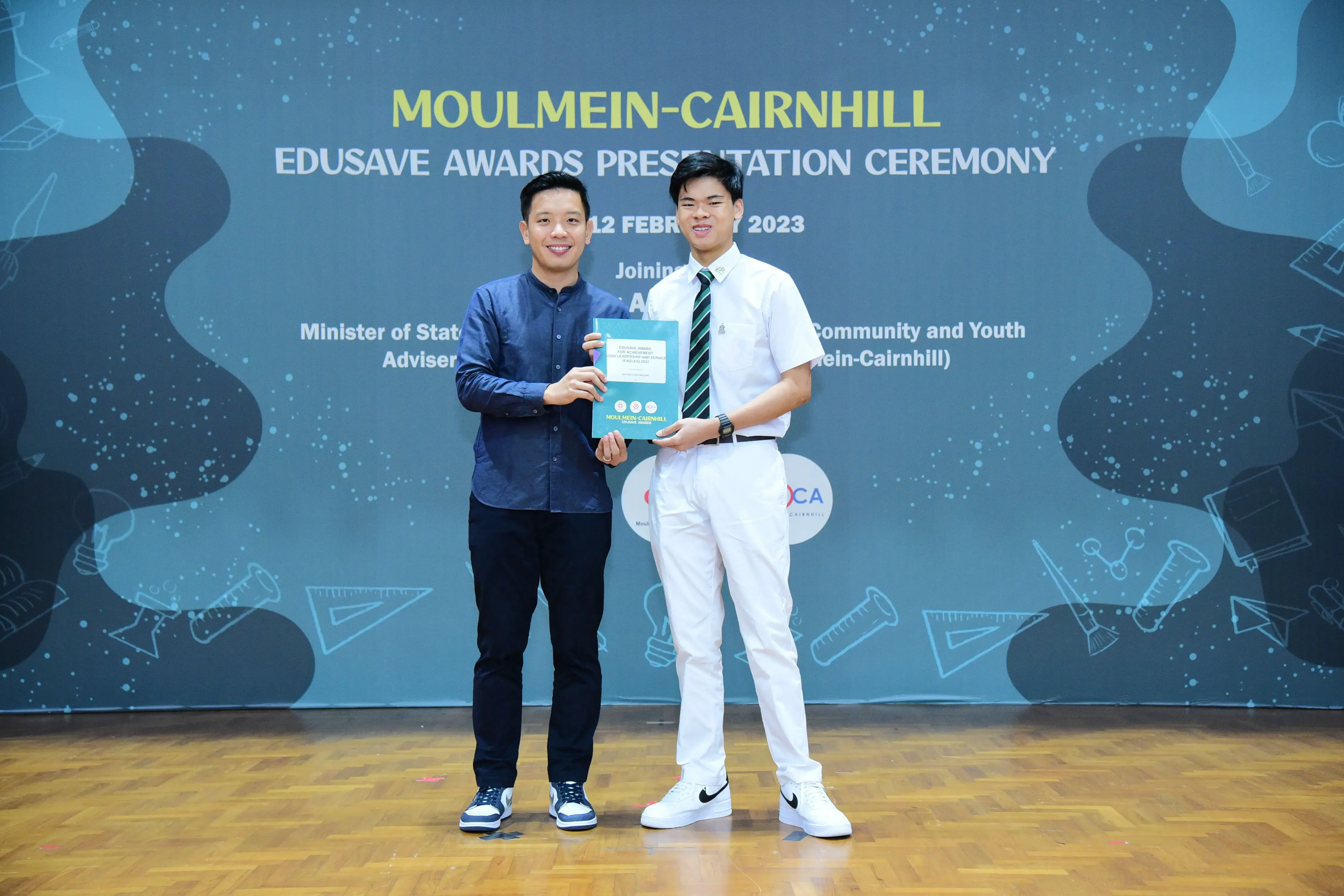 Two men hold a certificate together at the Moulmein-Cairnhill Edusave Awards Presentation Ceremony on 12 February 2023.