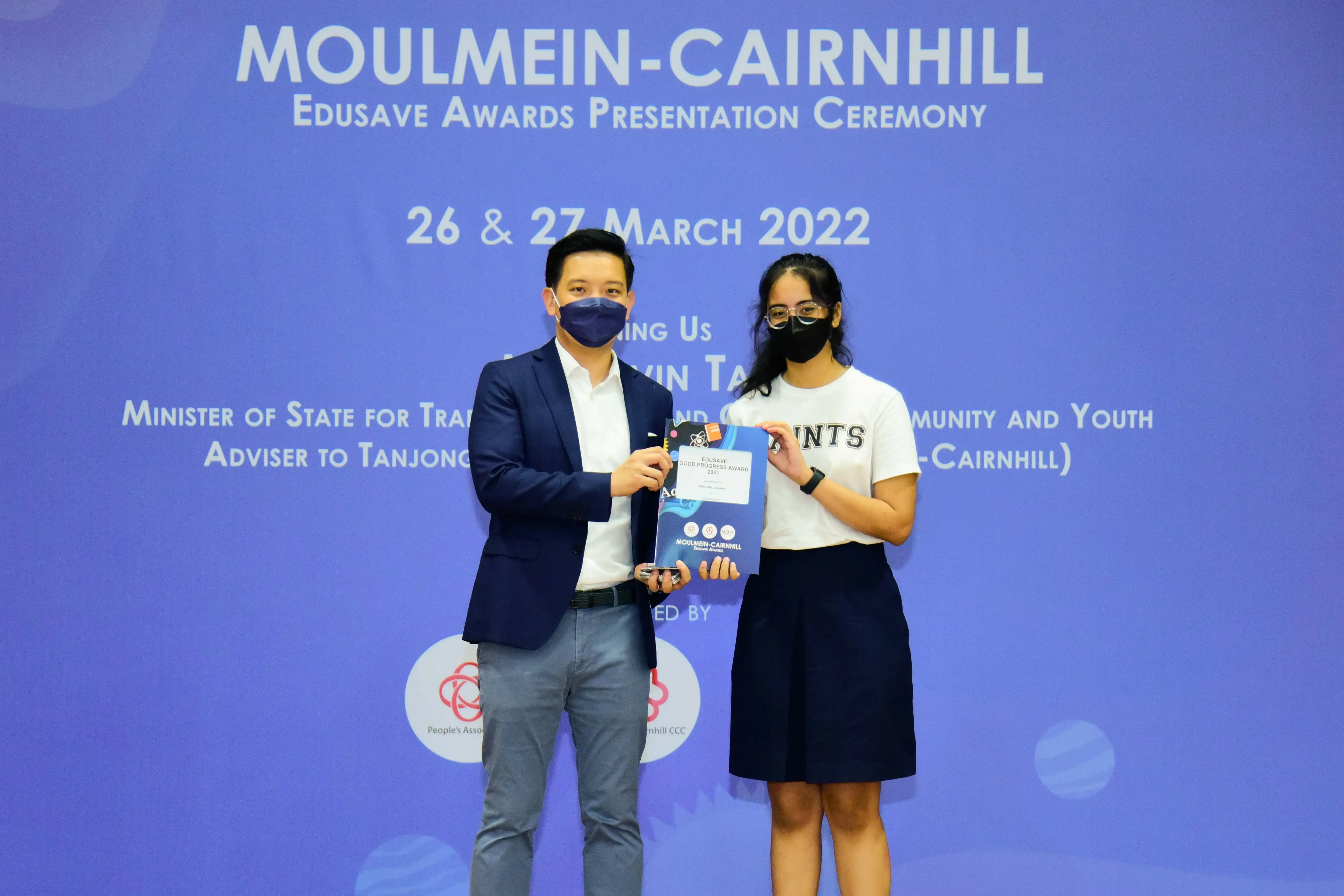 Two masked people hold an award certificate at the Moulmein-Cairnhill Edusave Awards Presentation Ceremony, March 2022.
