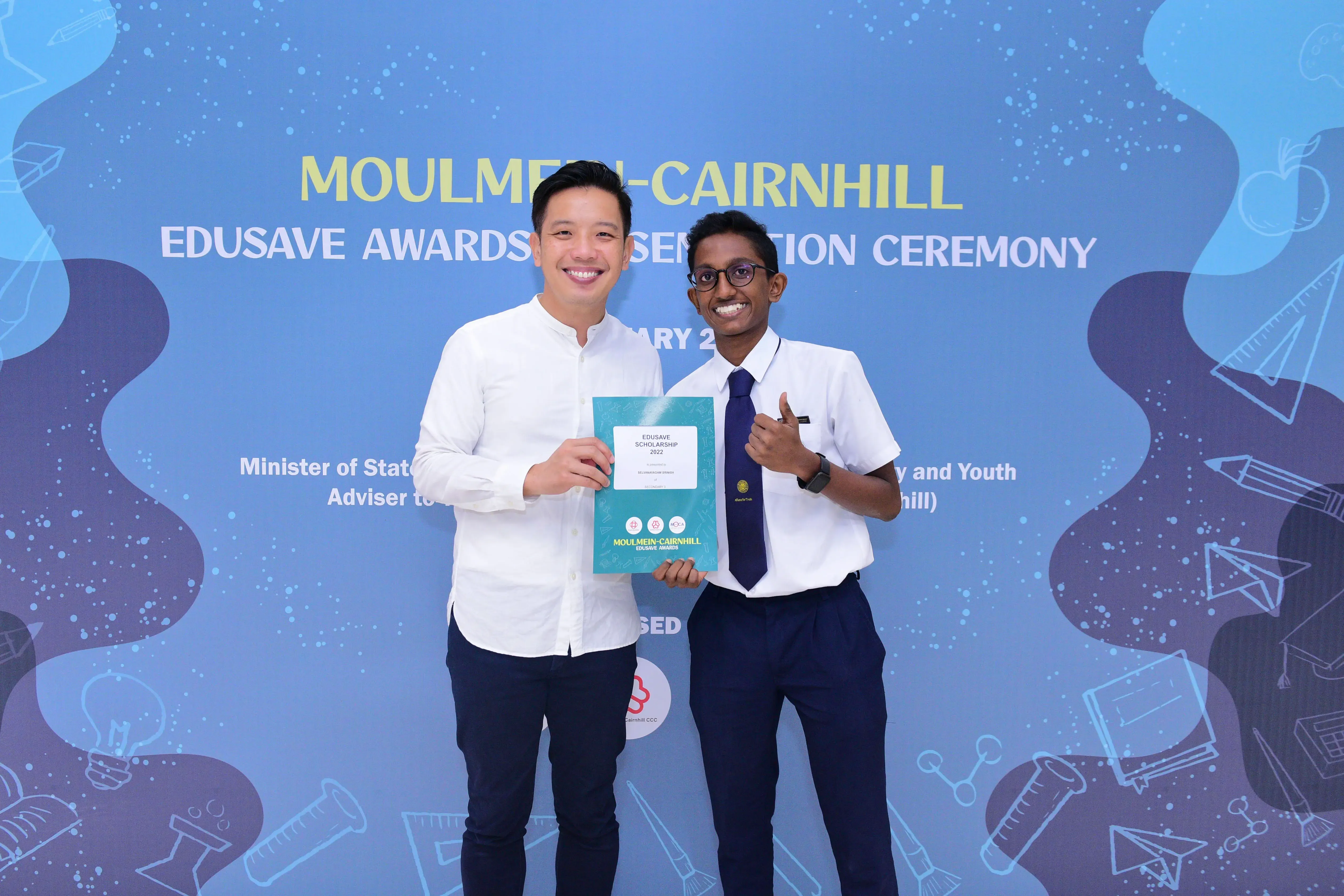 Two men smile holding an Edusave Scholarship certificate at the Moulmein-Cairnhill Edusave Awards Presentation Ceremony.