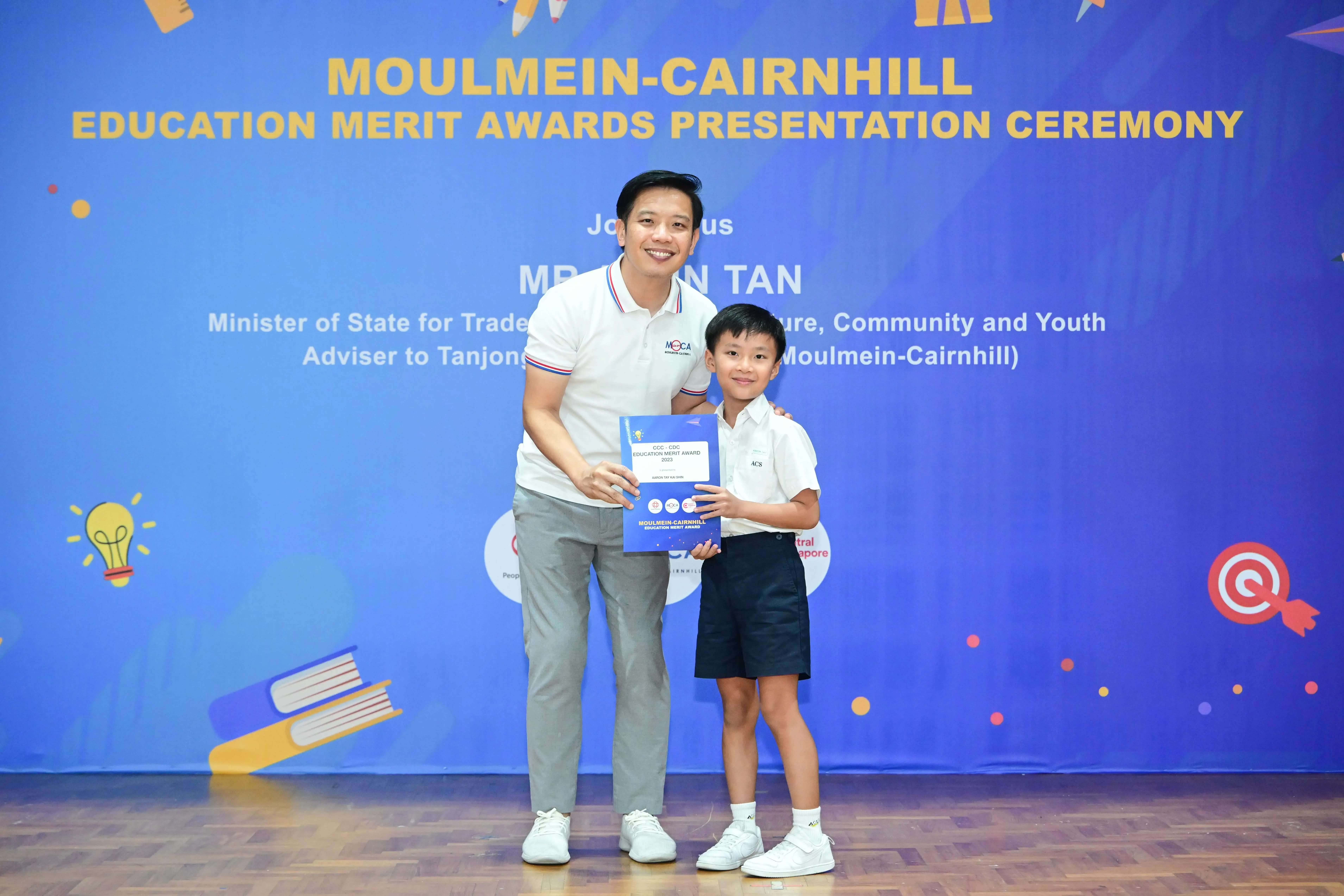 A man and a young boy hold an award certificate at the Moulmein-Cairnhill Education Merit Awards Presentation Ceremony.
