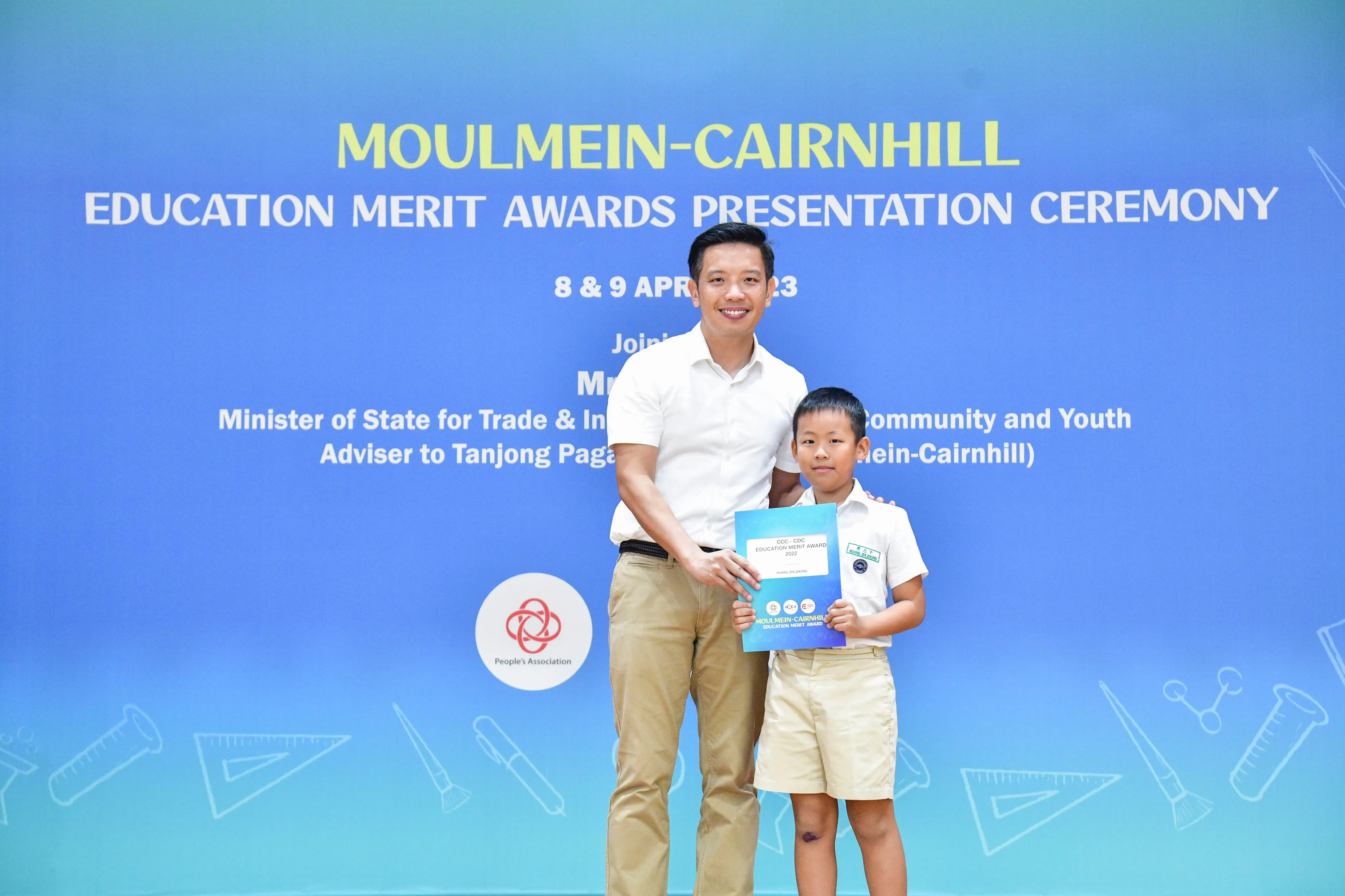 A man and young boy pose holding an award certificate at the Moulmein-Cairnhill Education Merit Awards Ceremony.