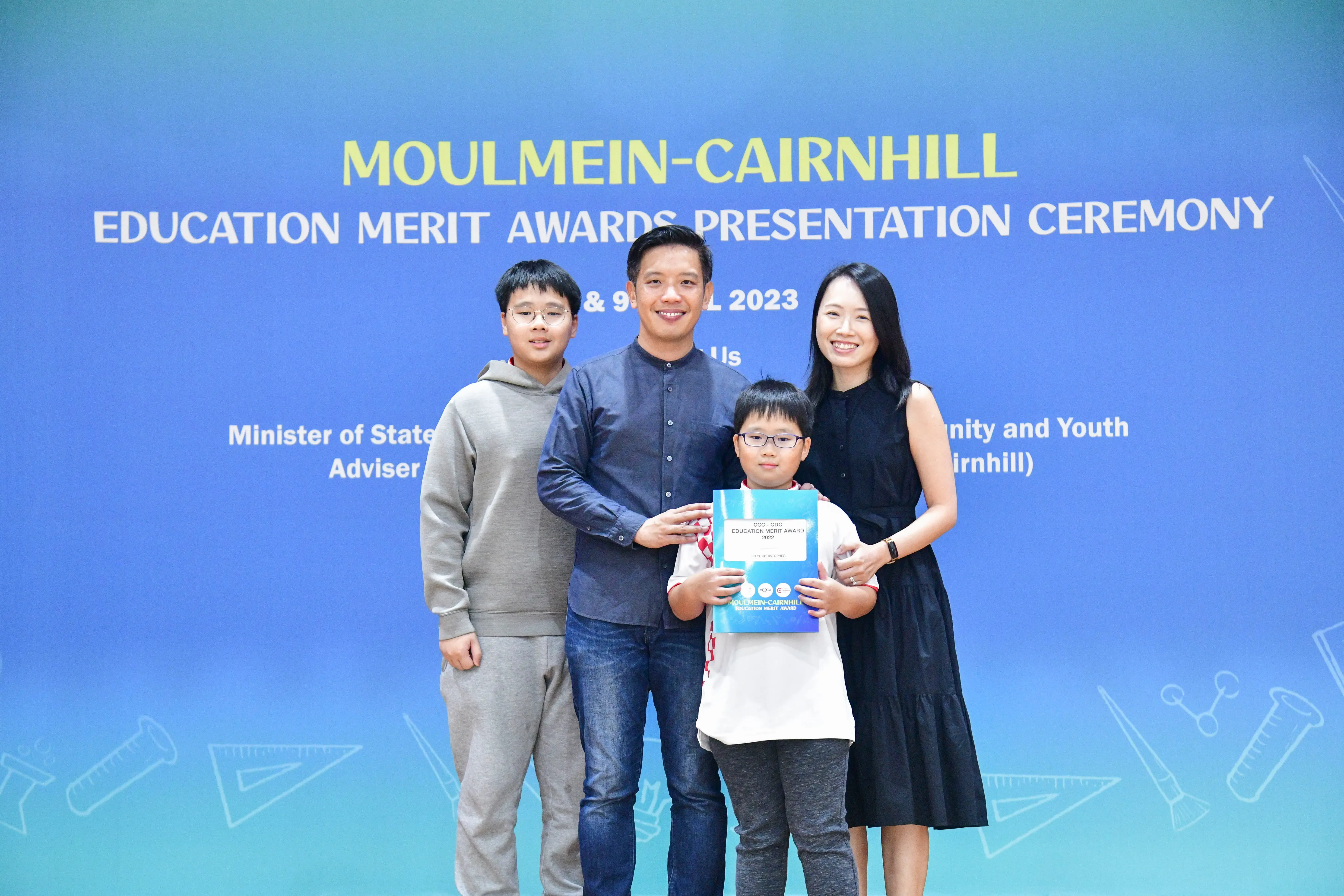 Family of four posing at the Moulmein-Cairnhill Education Merit Awards Ceremony 2023, child holding an award folder.