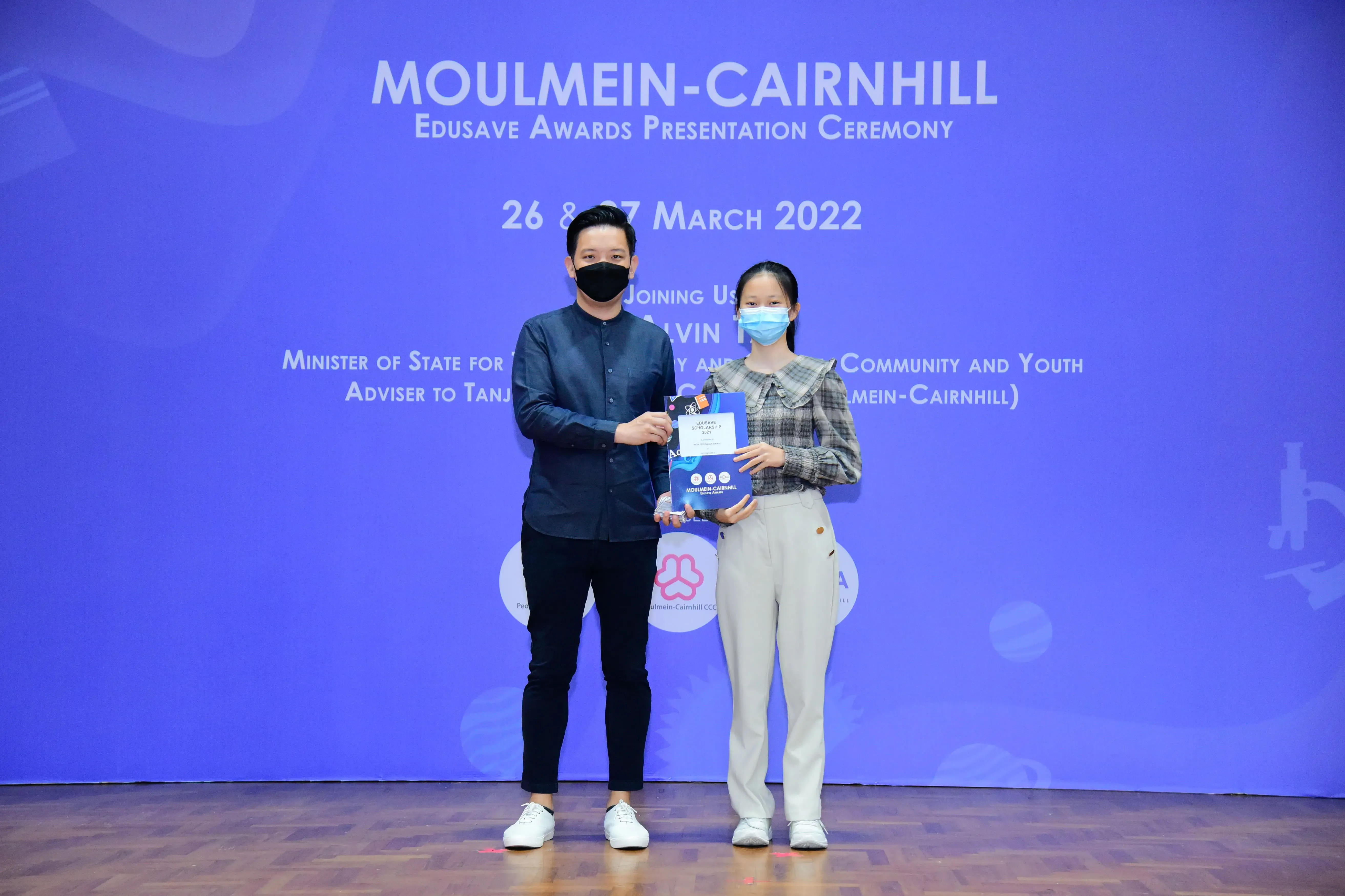Two masked people hold an award certificate at the Moulmein-Cairnhill Edusave Awards Ceremony, March 2022.