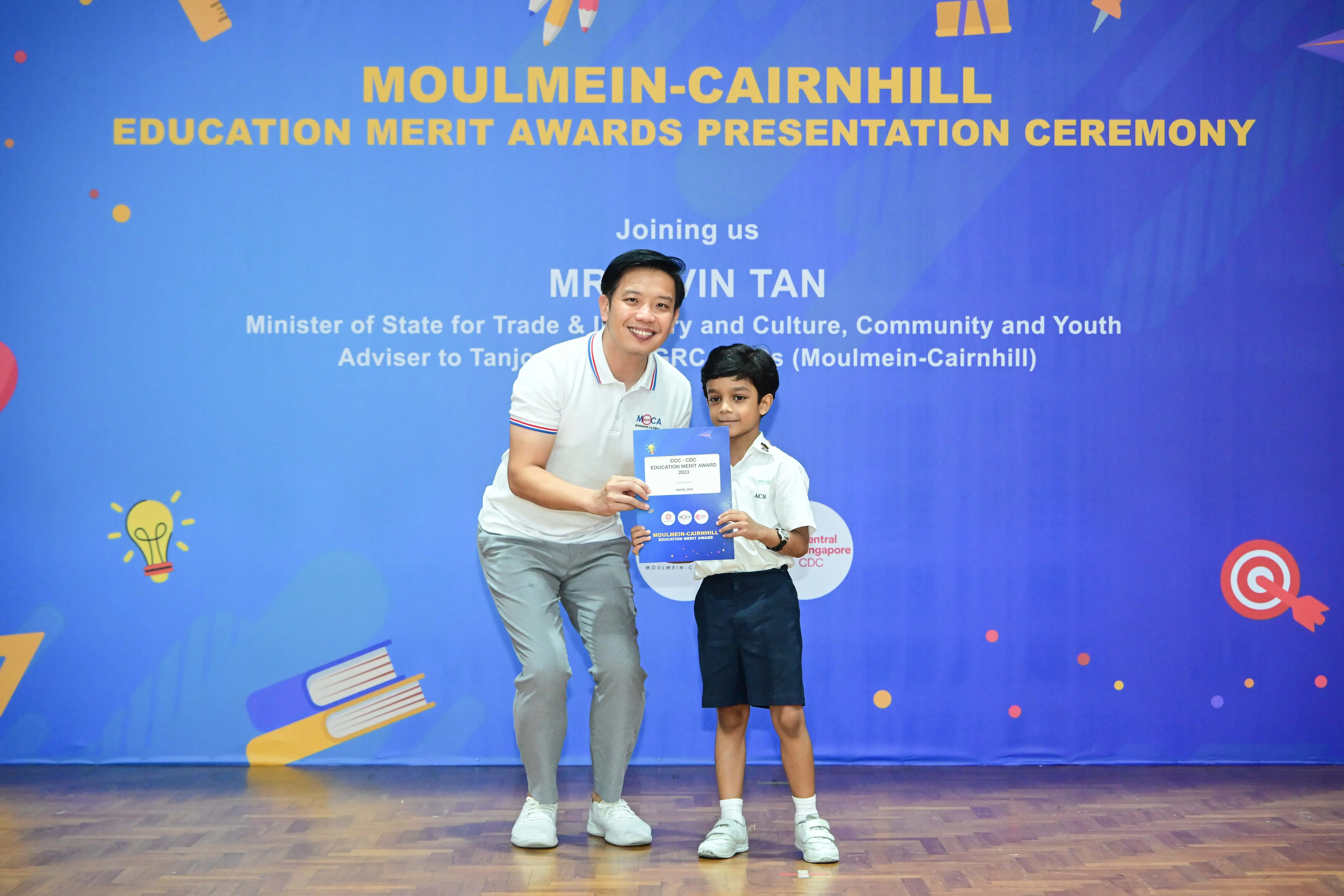 A man and a young boy hold an award certificate at the Moulmein-Cairnhill Education Merit Awards ceremony.