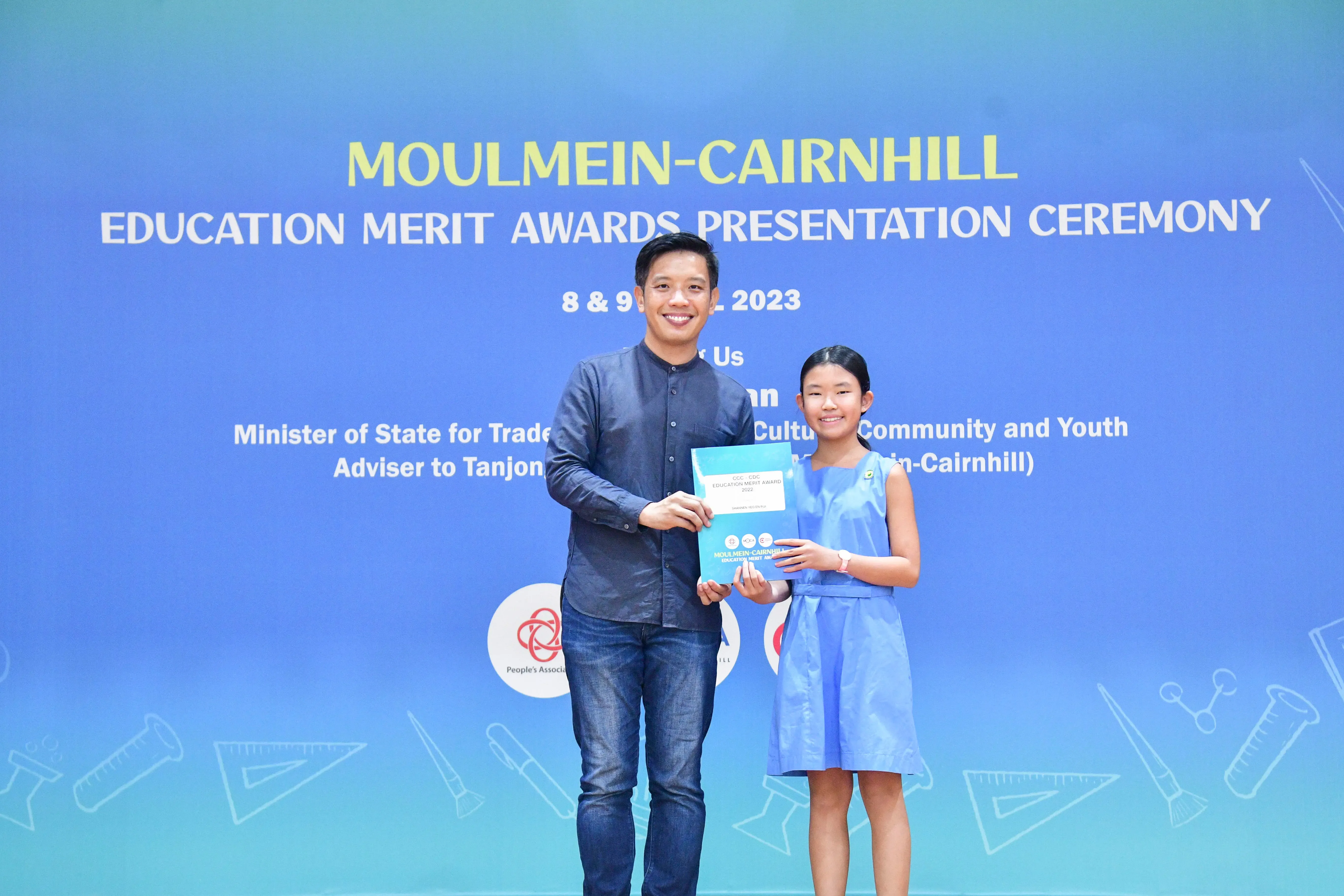 A man and a young girl hold an award certificate at the Moulmein-Cairnhill Education Merit Awards Ceremony 2023.