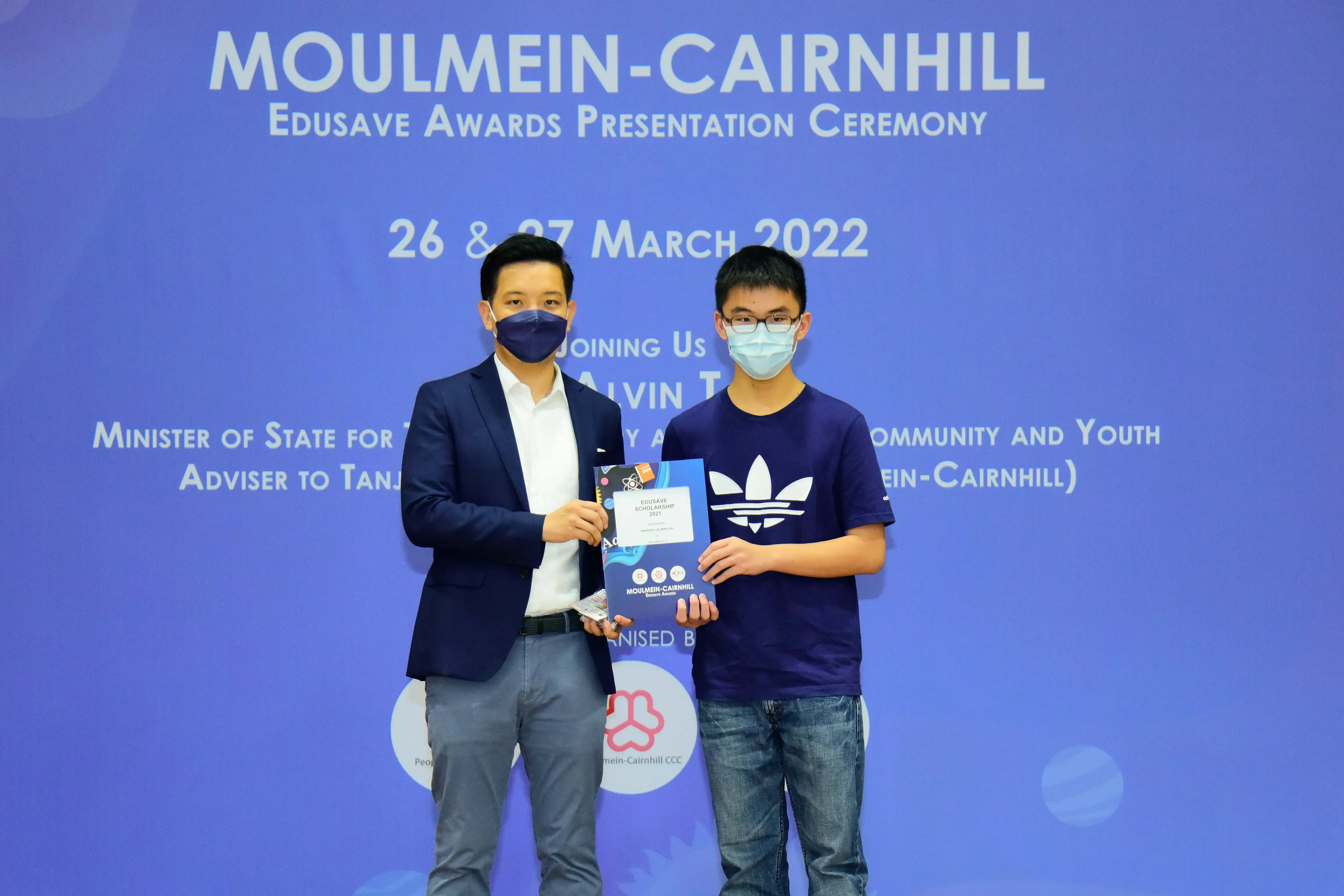 Two masked men hold an award at the Moulmein-Cairnhill Edusave Awards Presentation Ceremony, March 2022.