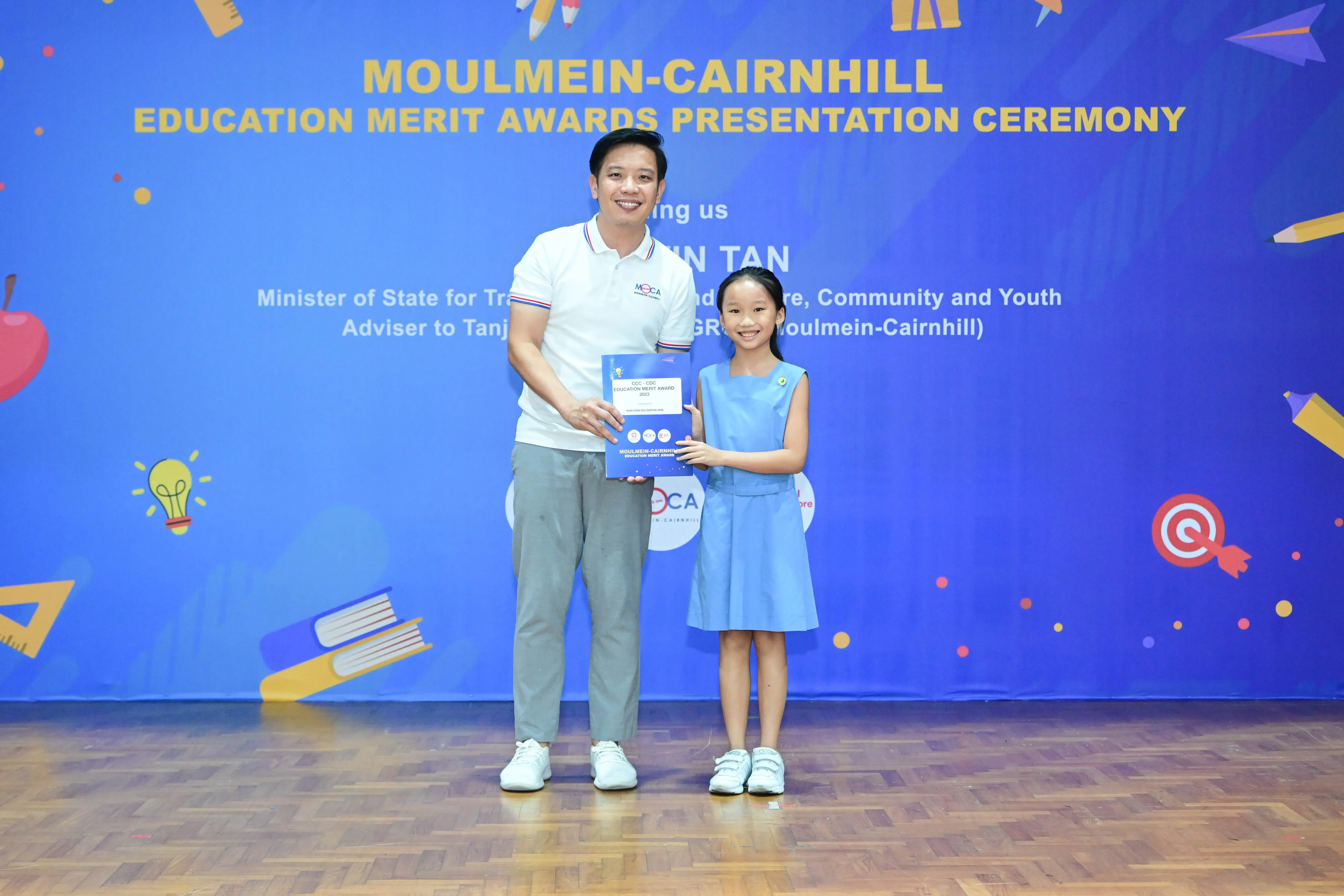 A man and a young girl hold an award certificate together at the Moulmein-Cairnhill Education Merit Awards Ceremony.