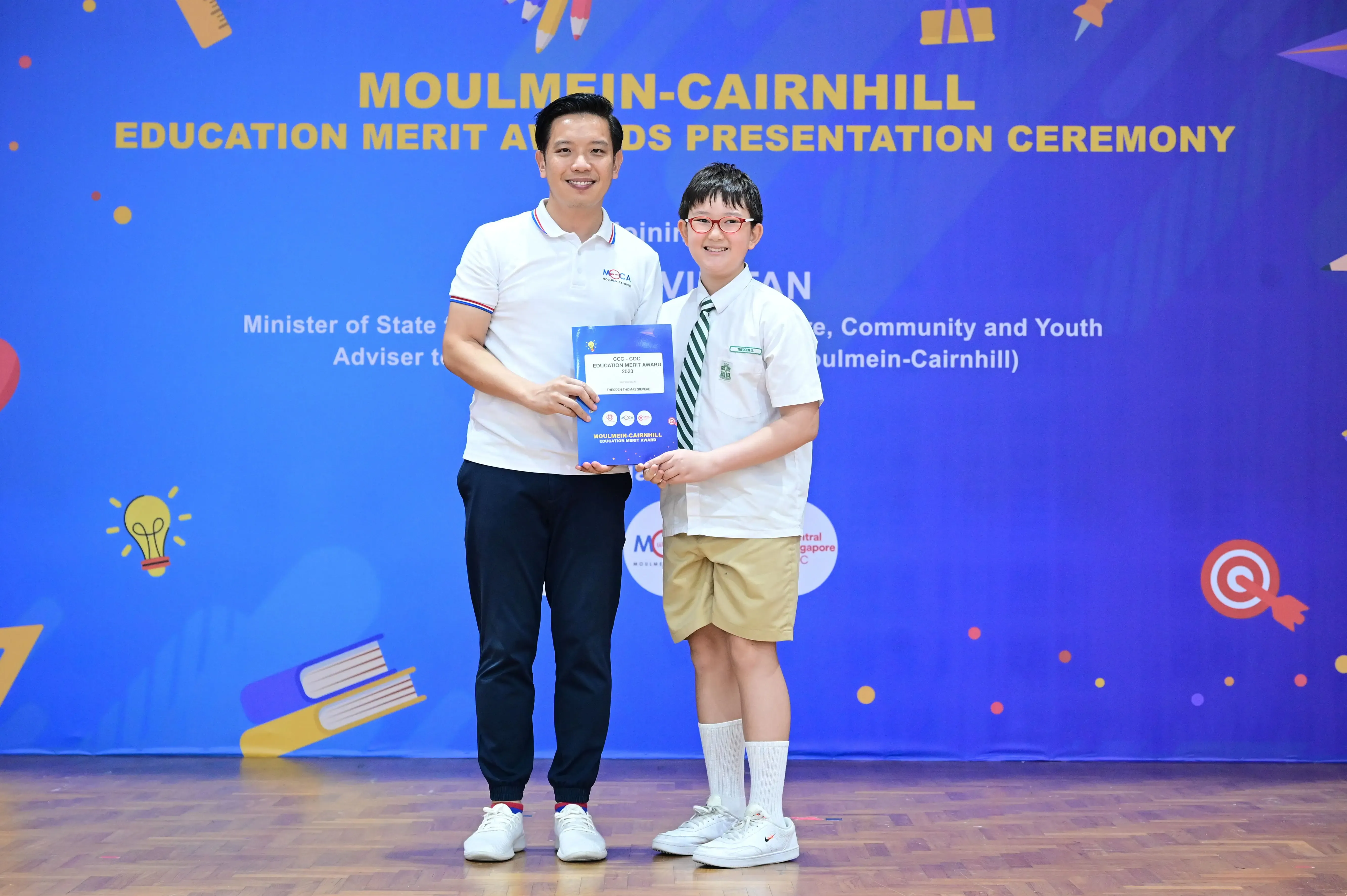 An adult and a uniformed student hold a certificate at the Moulmein-Cairnhill Education Merit Awards ceremony.