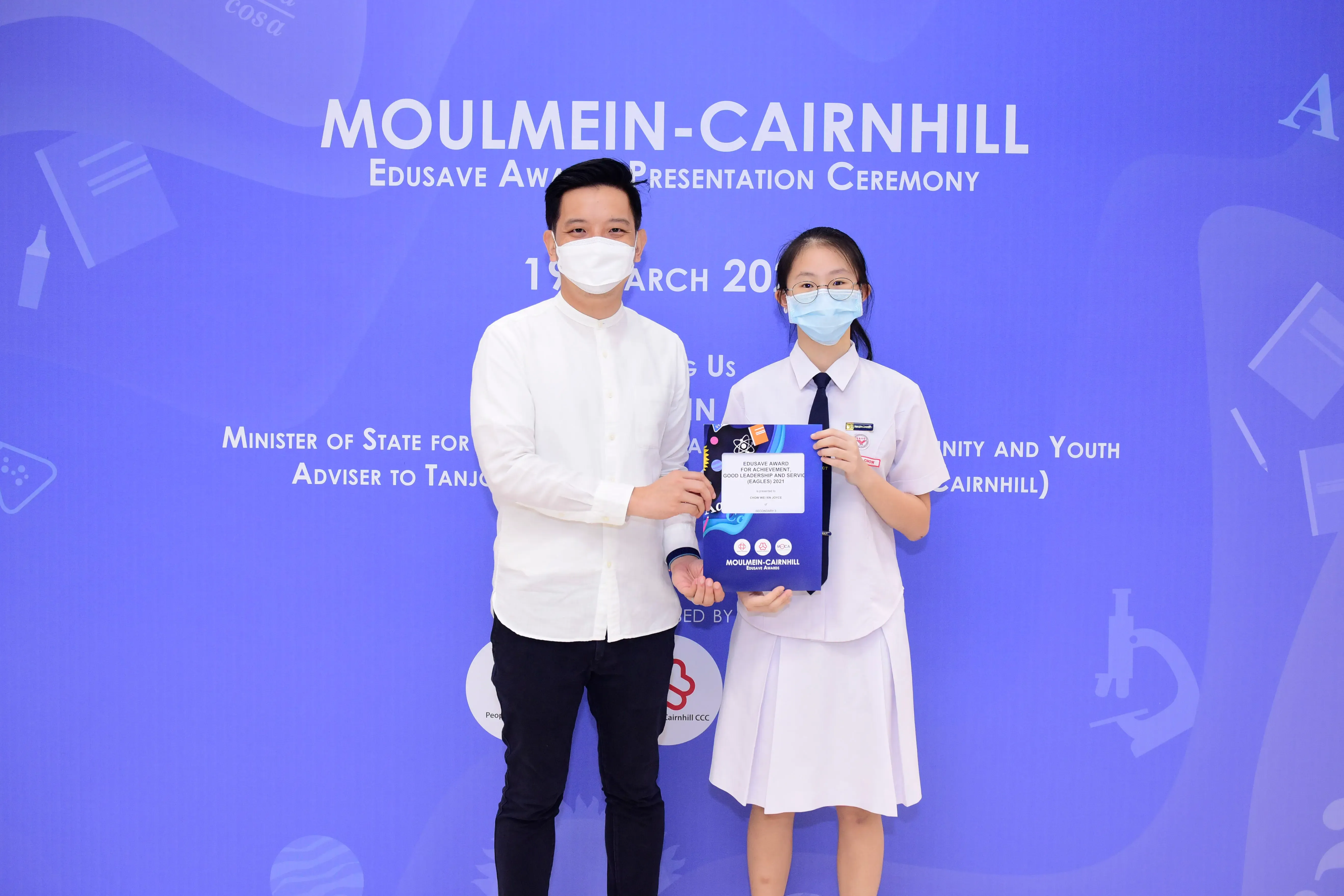 Two masked people pose at the Moulmein-Cairnhill Edusave Award Presentation Ceremony, student holds an award.