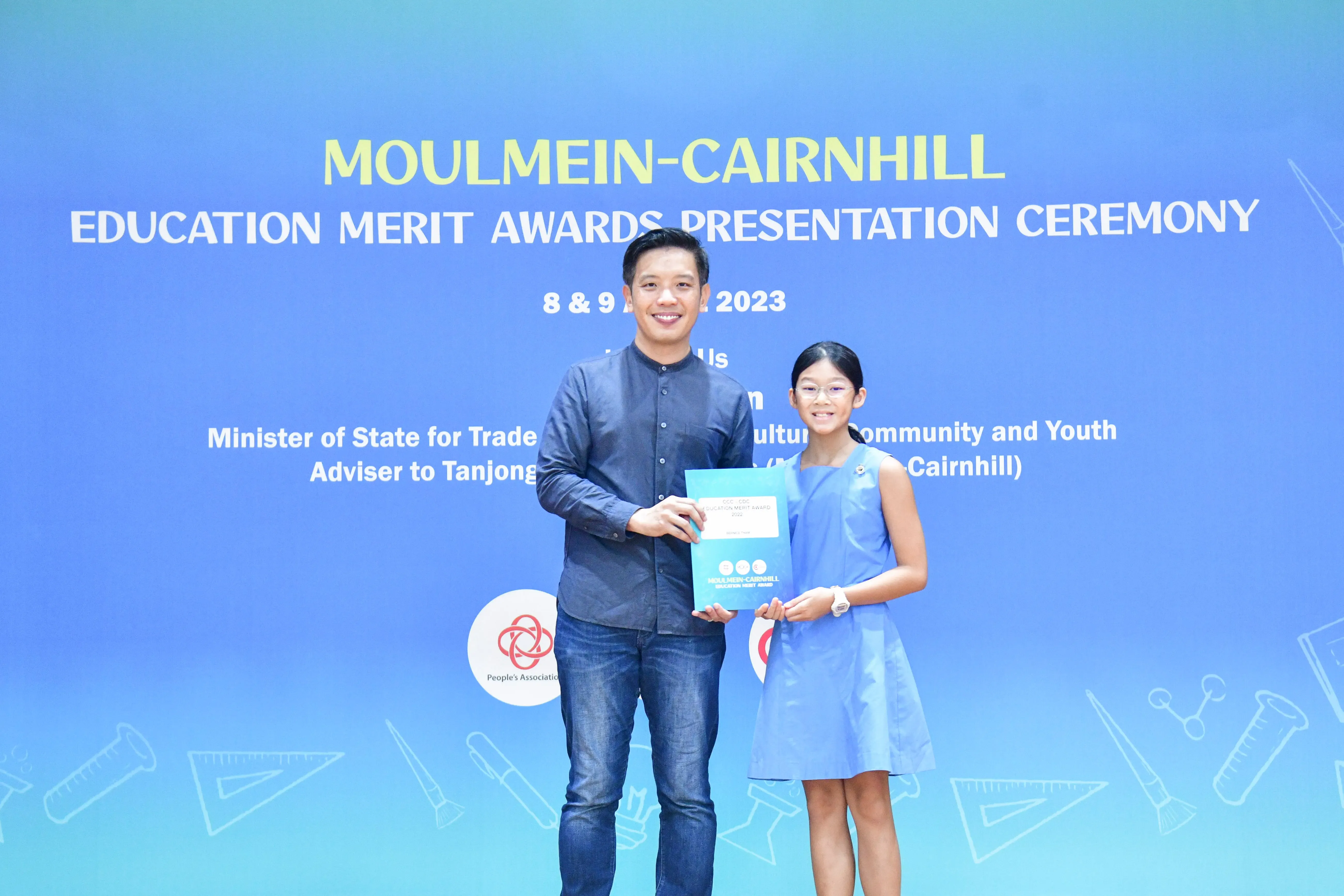 A man and a young girl hold a certificate together at the Moulmein-Cairnhill Education Merit Awards Ceremony 2023.
