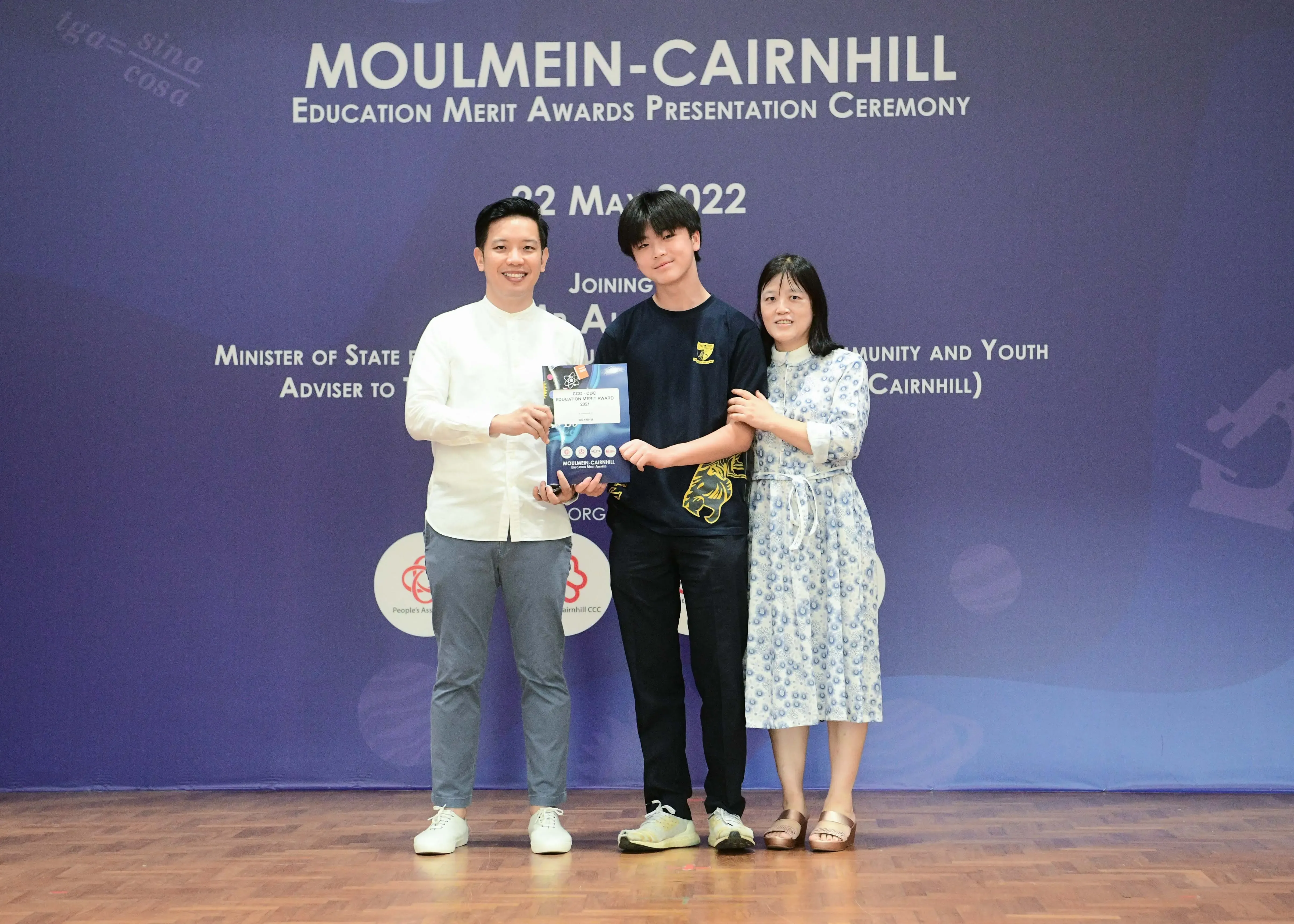 Three people pose holding an award certificate at the Moulmein-Cairnhill Education Merit Awards Ceremony on 22 May 2022.