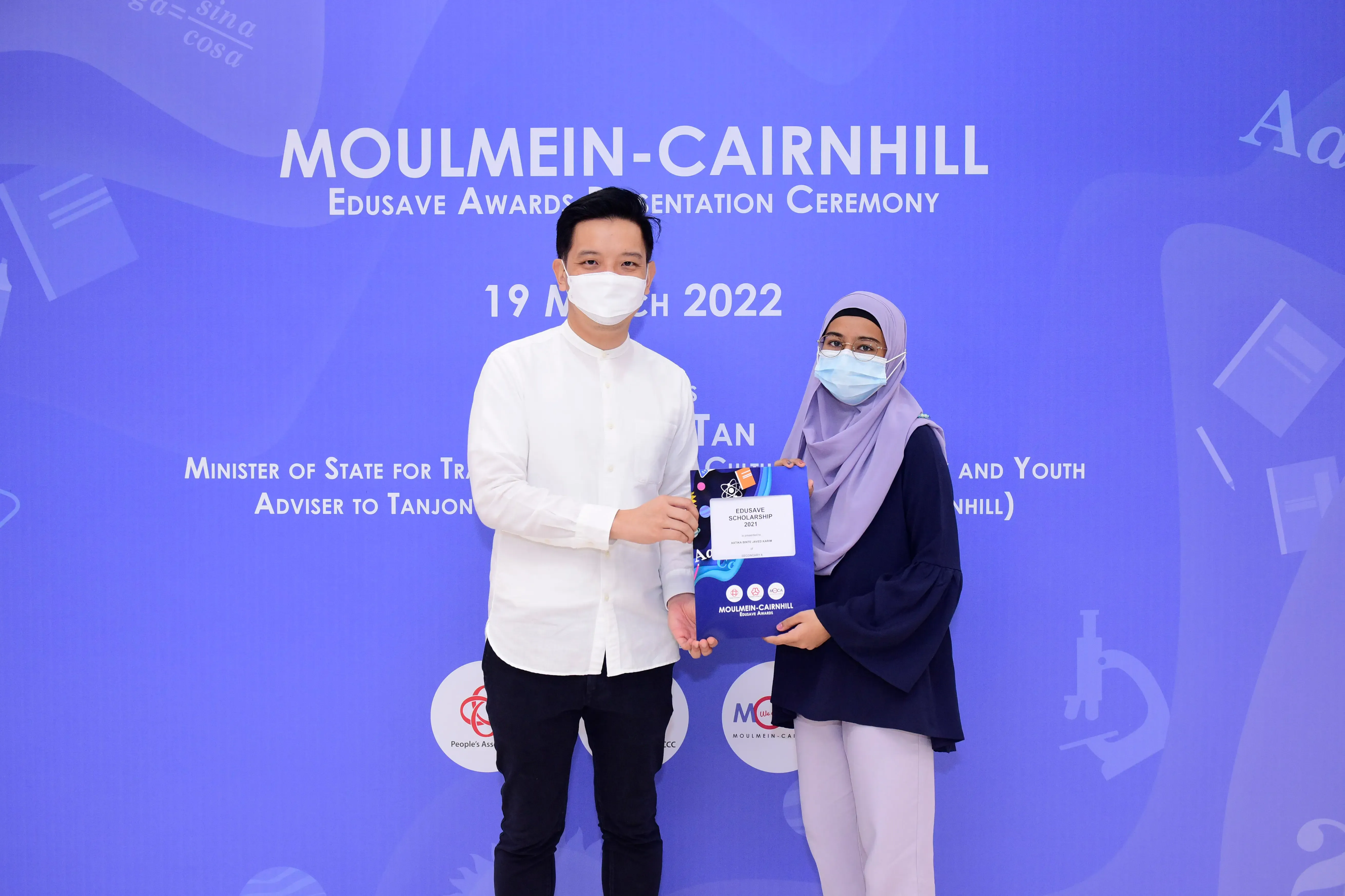 Two masked people holding an Edusave Scholarship certificate at the Moulmein-Cairnhill Awards Ceremony, March 2022.