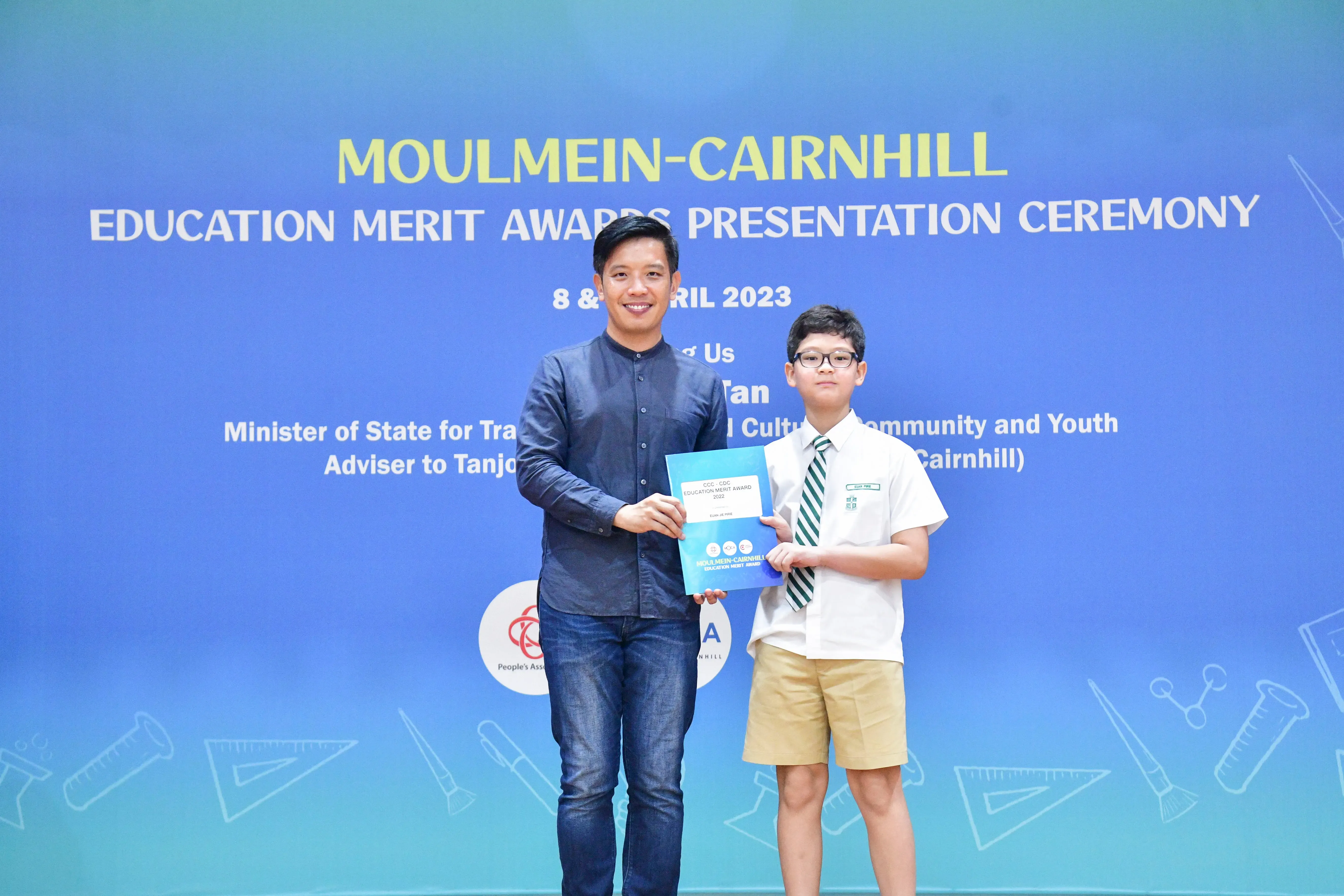 An adult and a young boy in school uniform hold a certificate at the Moulmein-Cairnhill Education Merit Awards 2023.