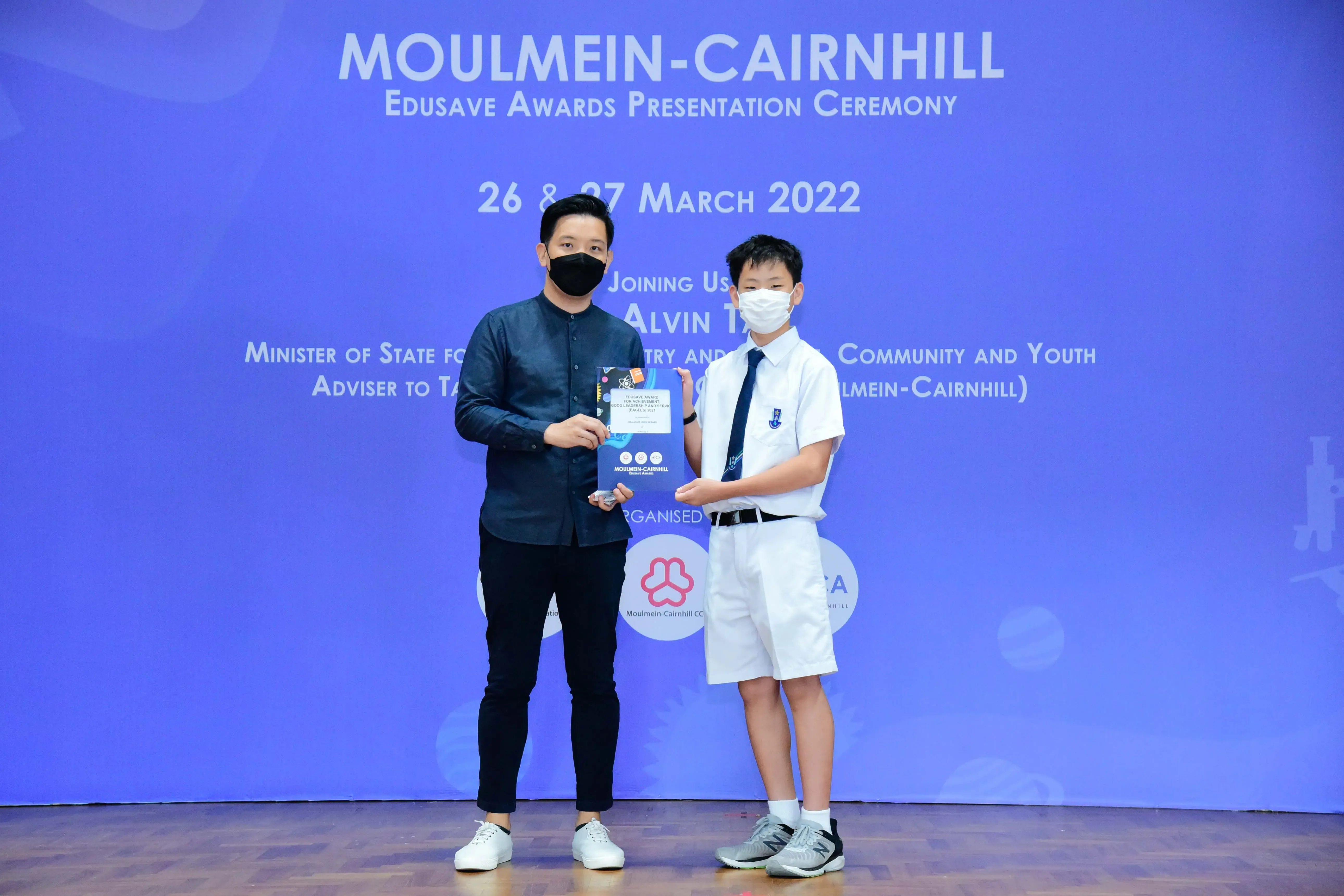 Two masked individuals hold an award at the Moulmein-Cairnhill Edusave Awards Ceremony on 26-27 March 2022.