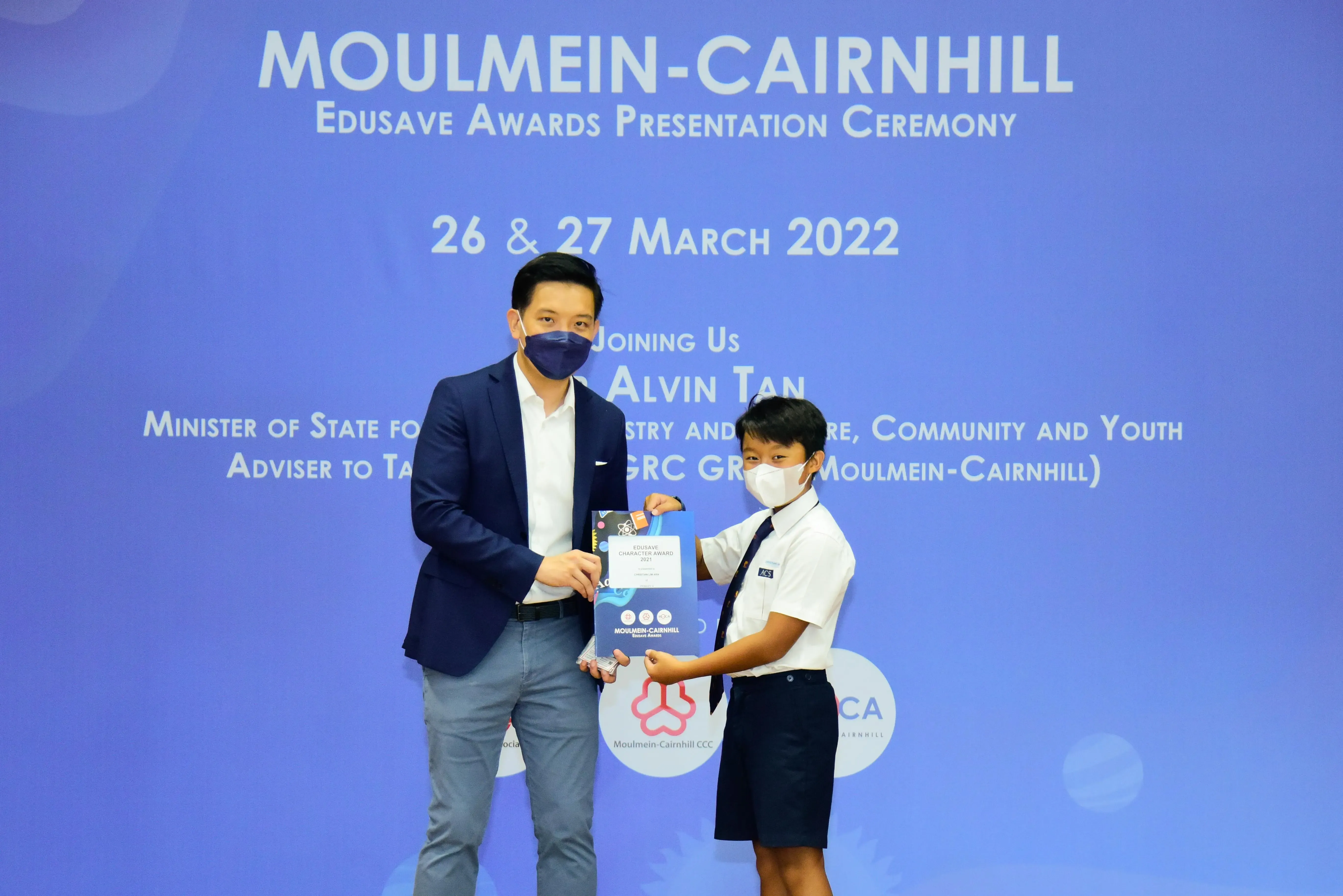 An adult in a blazer presents an award to a uniformed student at the Moulmein-Cairnhill Edusave Awards Ceremony 2022.