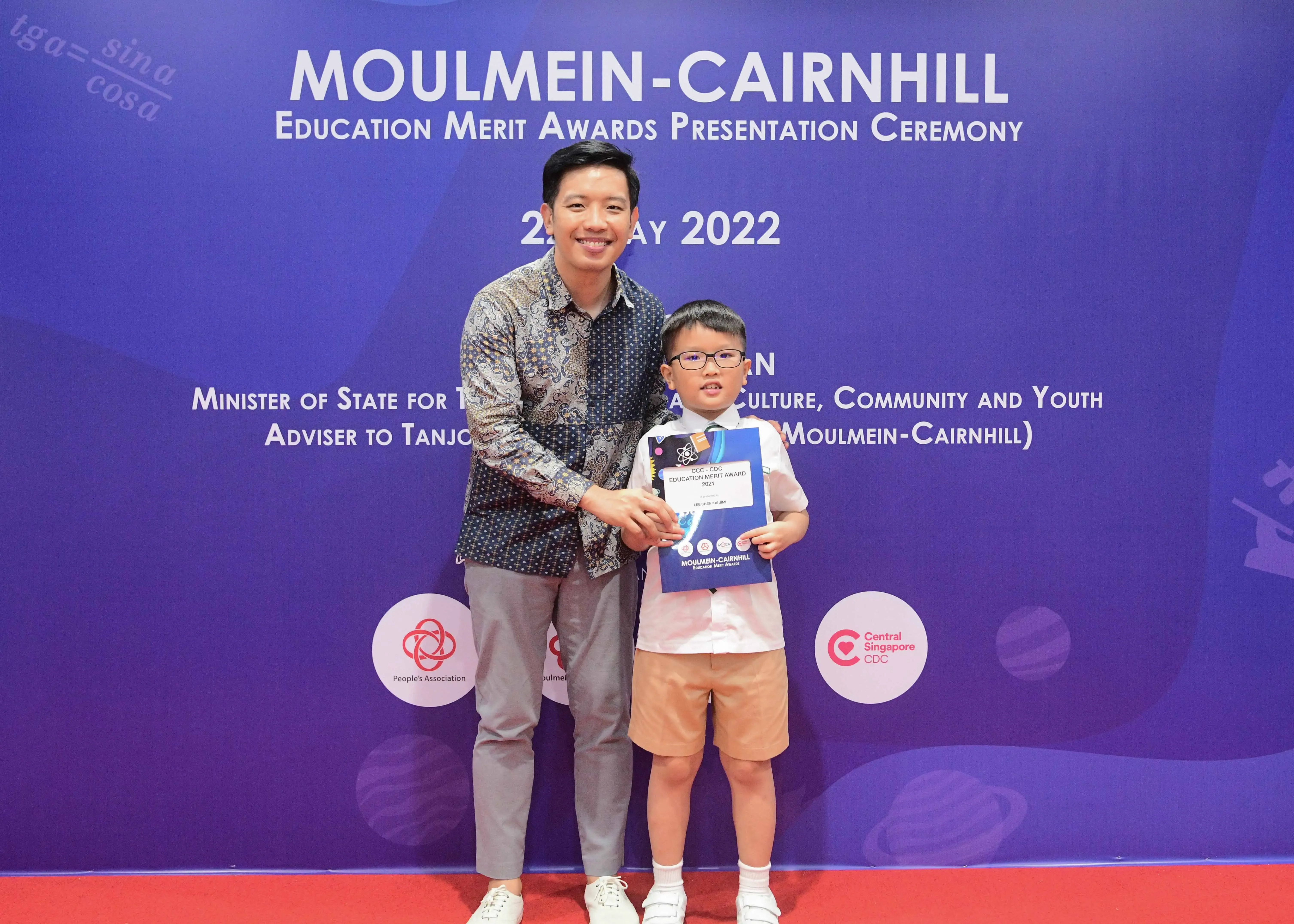 A man and a young boy holding an award certificate at the 2022 Moulmein-Cairnhill Education Merit Awards ceremony.