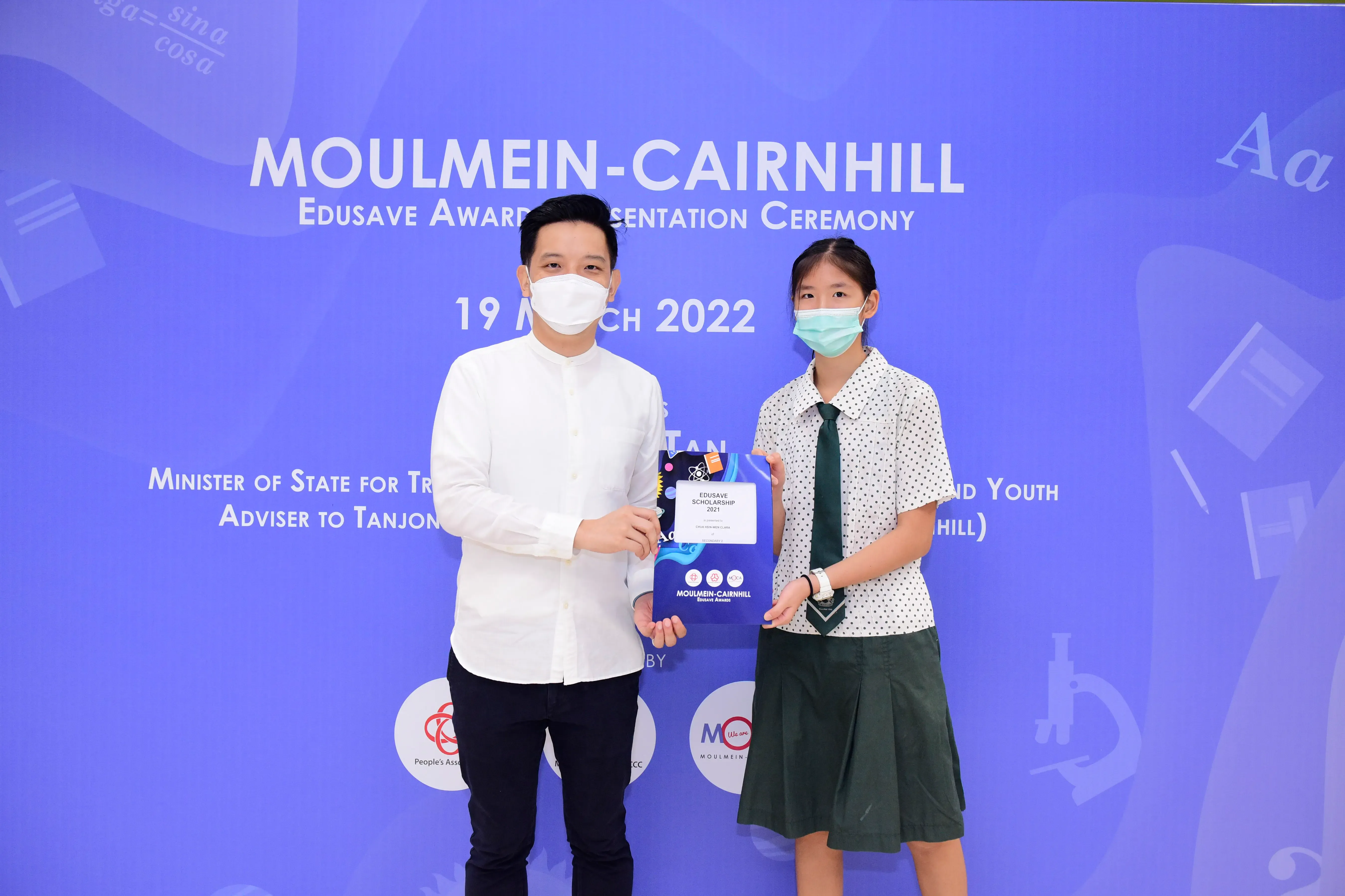Two masked individuals hold an Edusave Scholarship award at the Moulmein-Cairnhill ceremony on 19 March 2022.