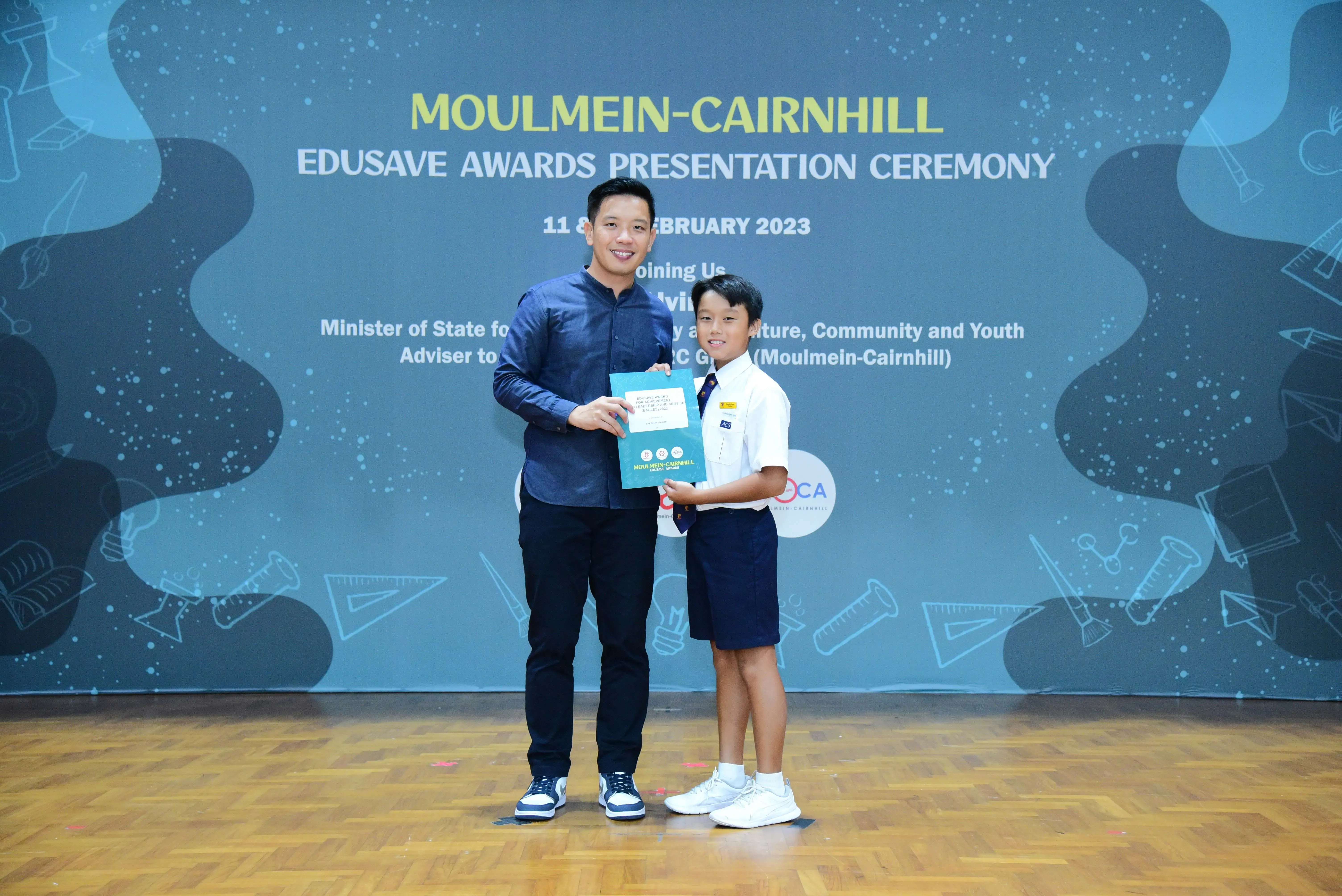 Adult and young student holding a certificate at Moulmein-Cairnhill Edusave Awards Presentation Ceremony, February 2023.