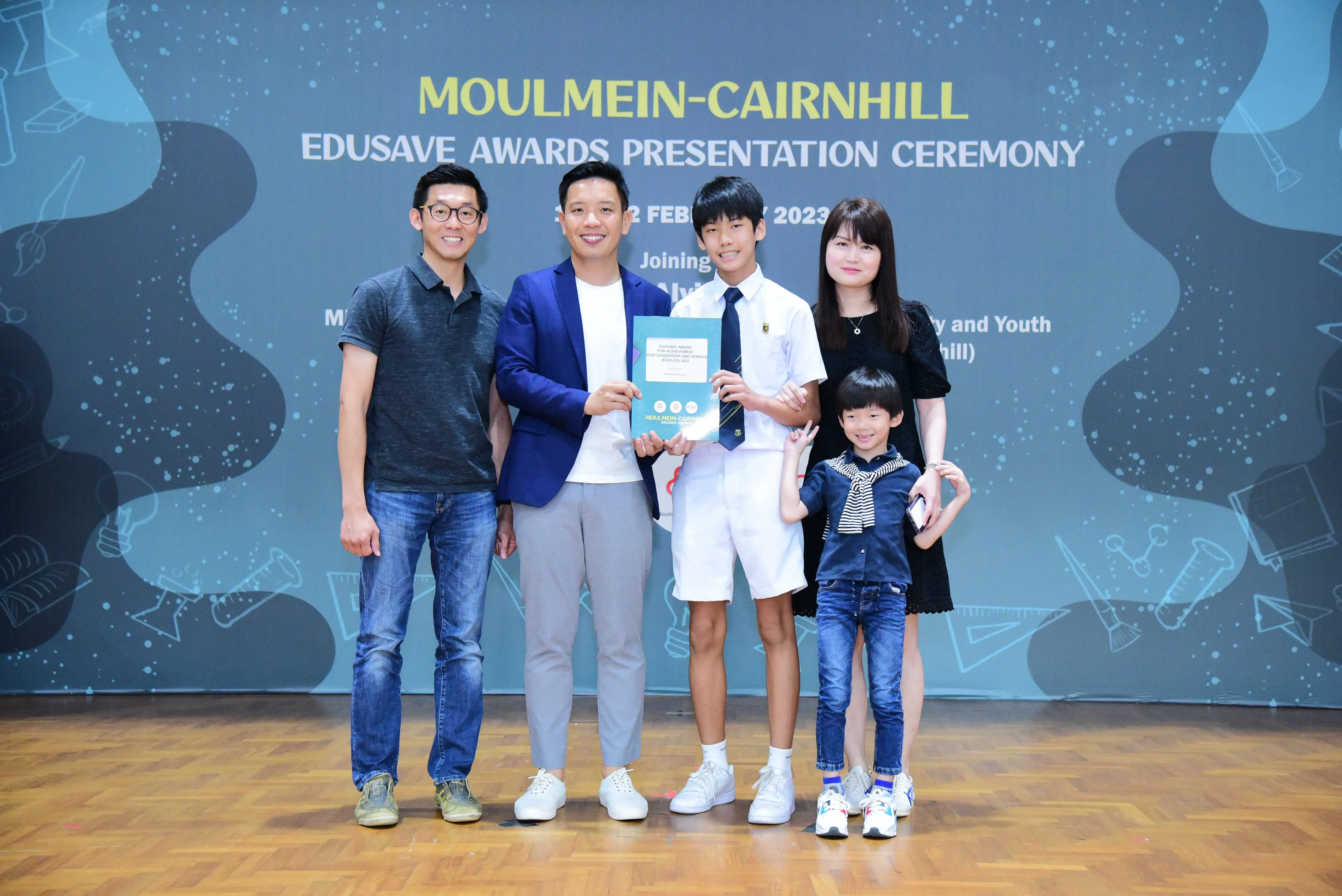 Five people pose at the Moulmein-Cairnhill Edusave Awards Presentation Ceremony 2023, with a student holding a certificate.