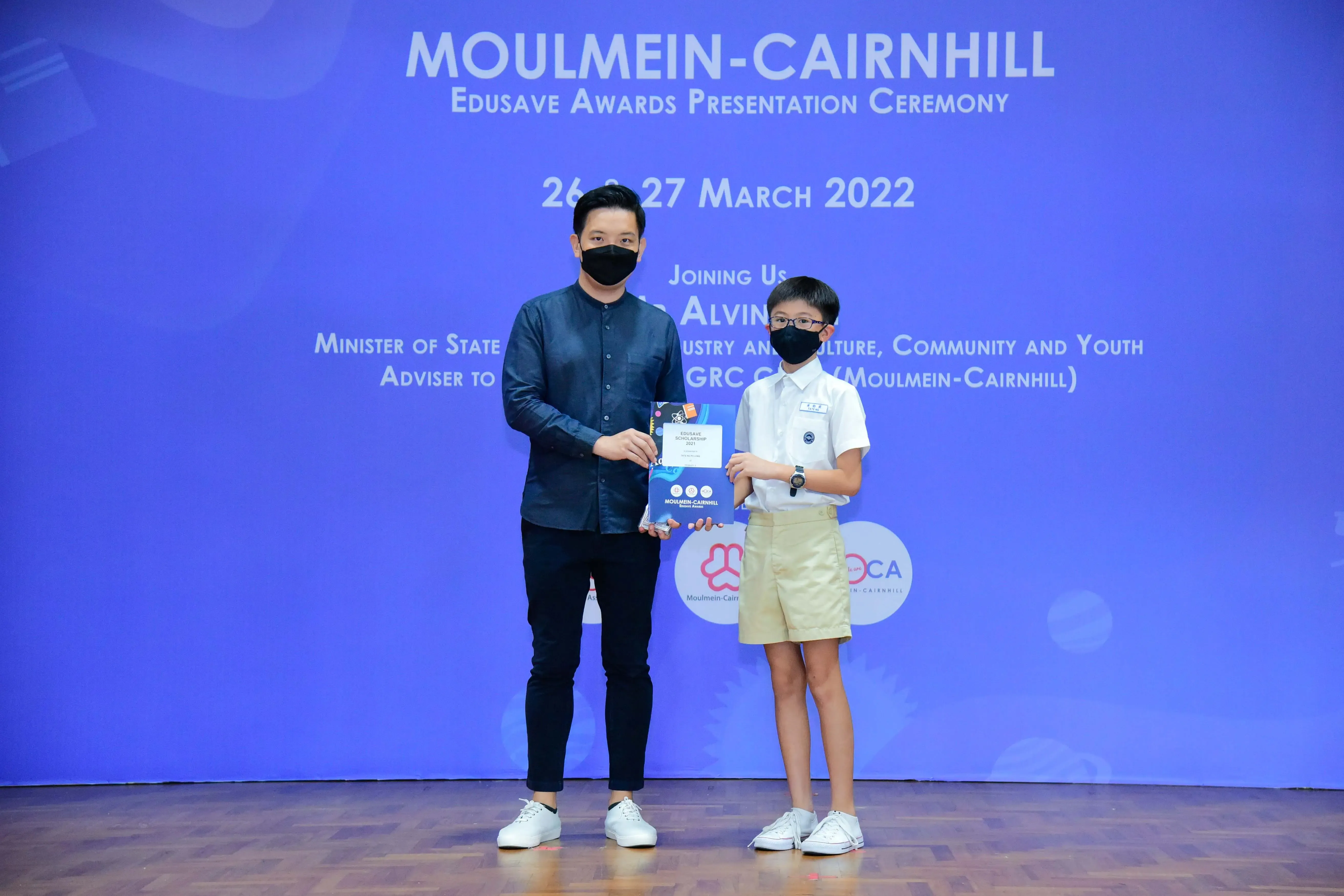 An adult and a young student in school uniform hold an award booklet at the Moulmein-Cairnhill Edusave Awards Ceremony 2022.