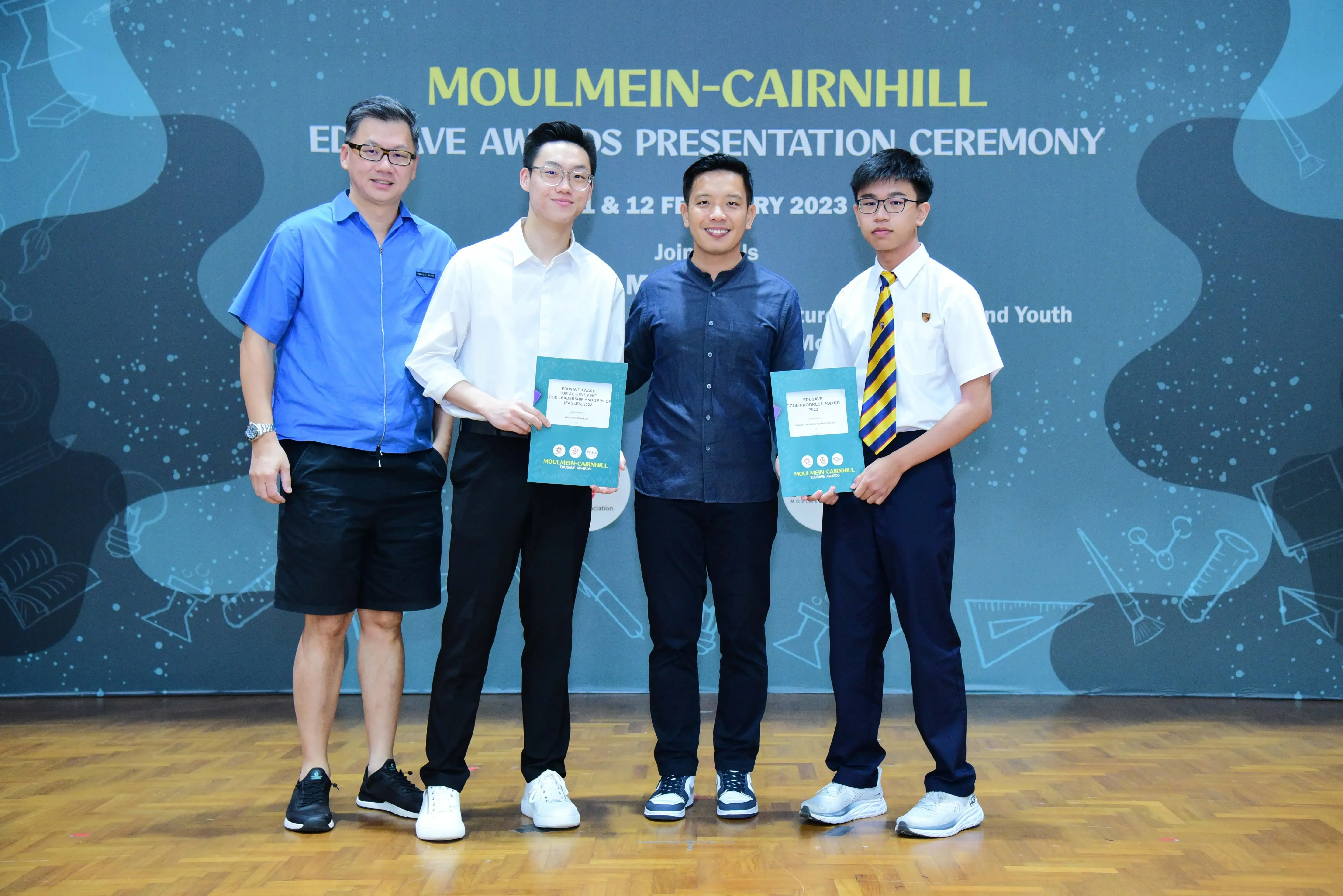 Four men pose at the Moulmein-Cairnhill Edusave Awards Presentation Ceremony 2023, two holding award certificates.