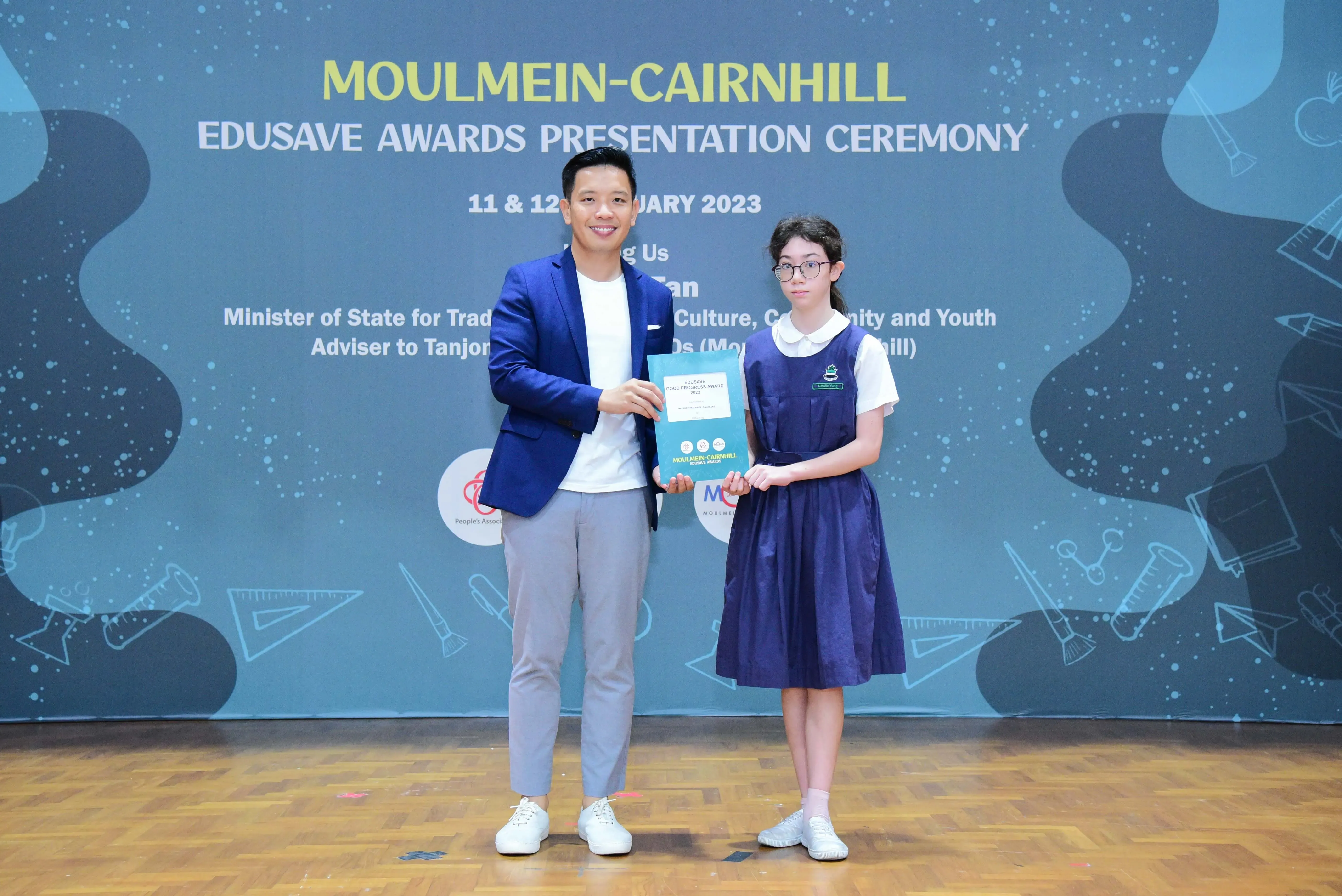 A man in a blue blazer and a girl in school uniform hold an award at the Moulmein-Cairnhill Edusave Awards Ceremony 2023.