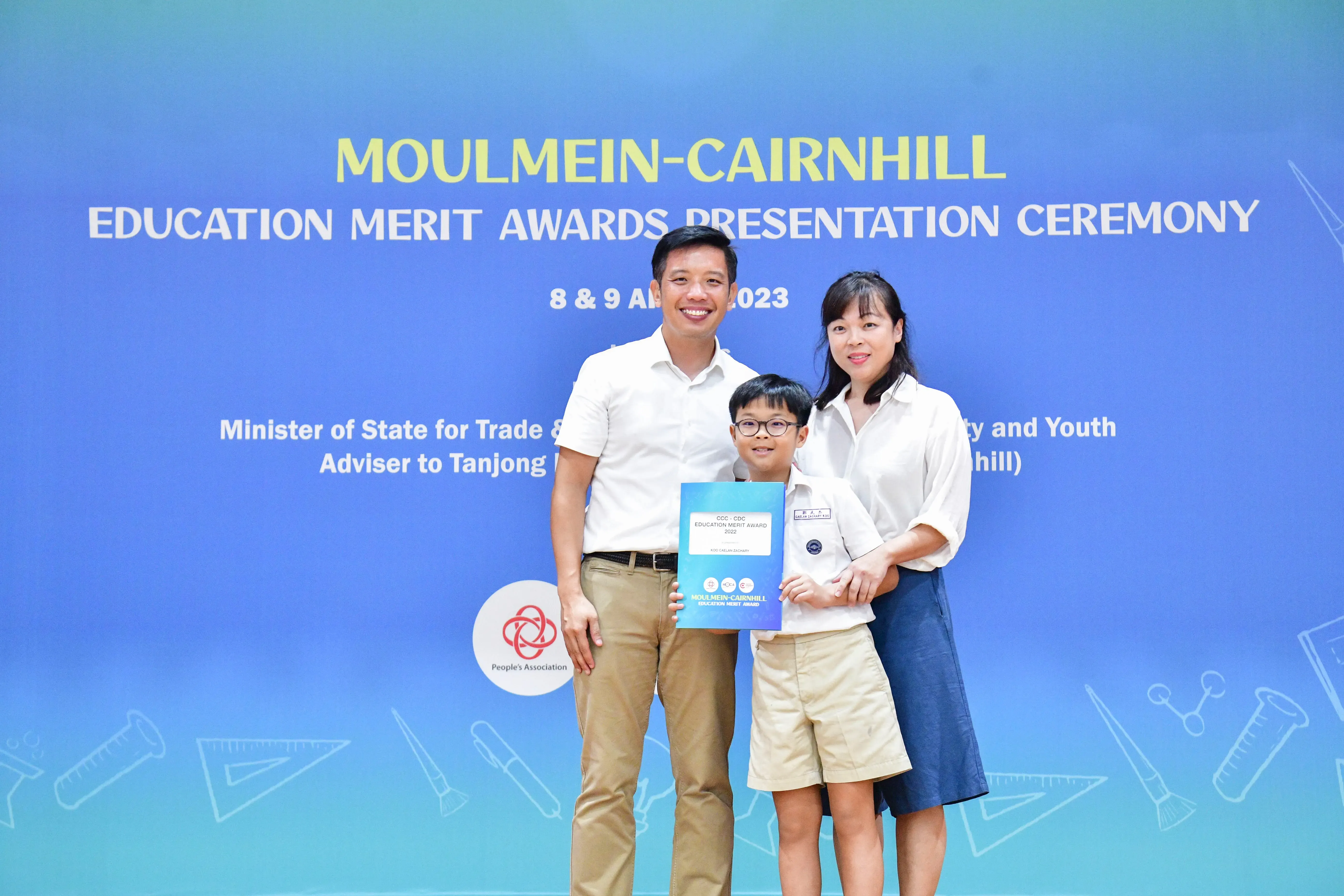 Two adults and a young boy holding a certificate pose at the Moulmein-Cairnhill Education Merit Awards 2023.