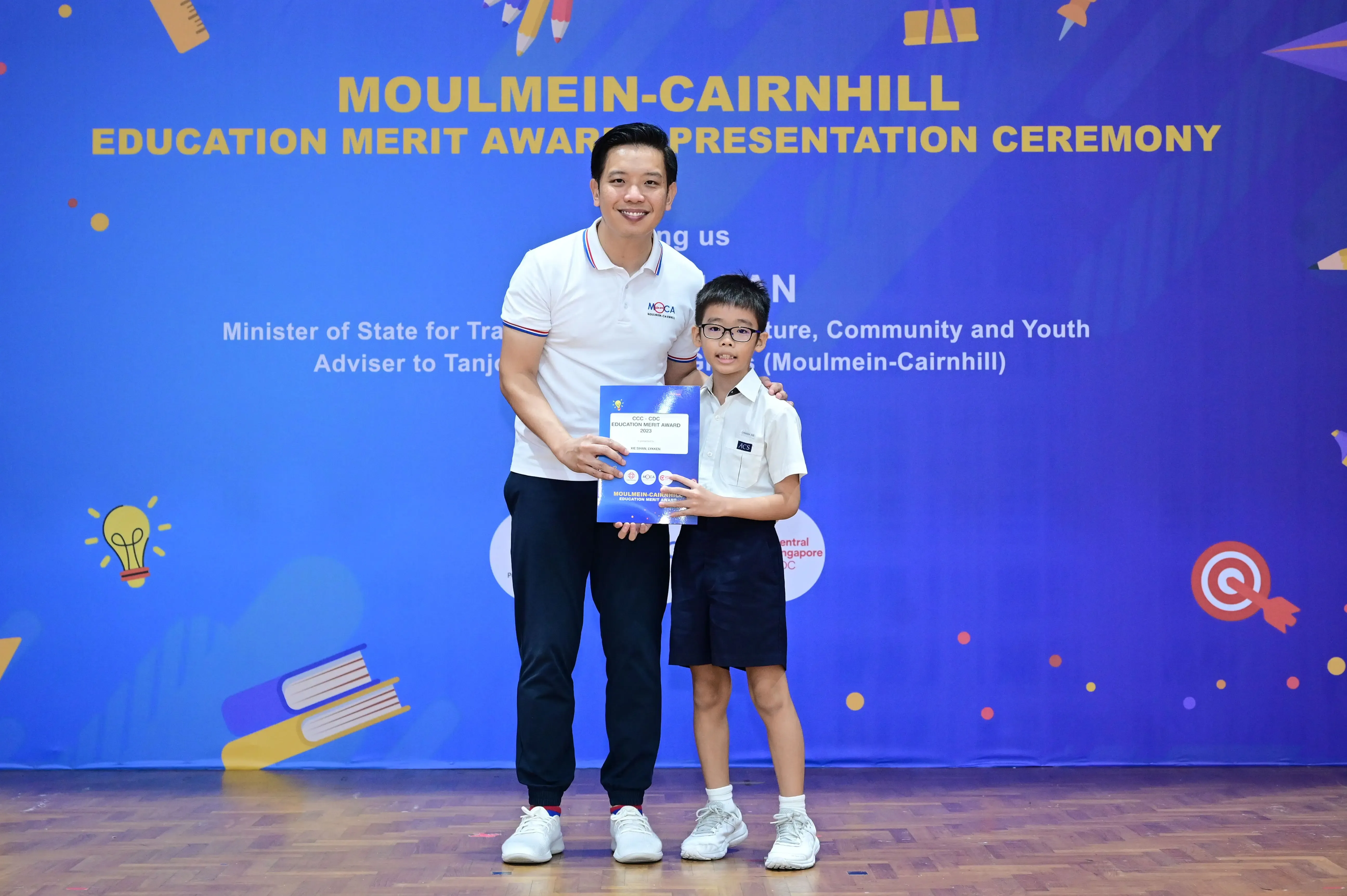 A man and a young boy holding a certificate at the Moulmein-Cairnhill Education Merit Award Presentation Ceremony.