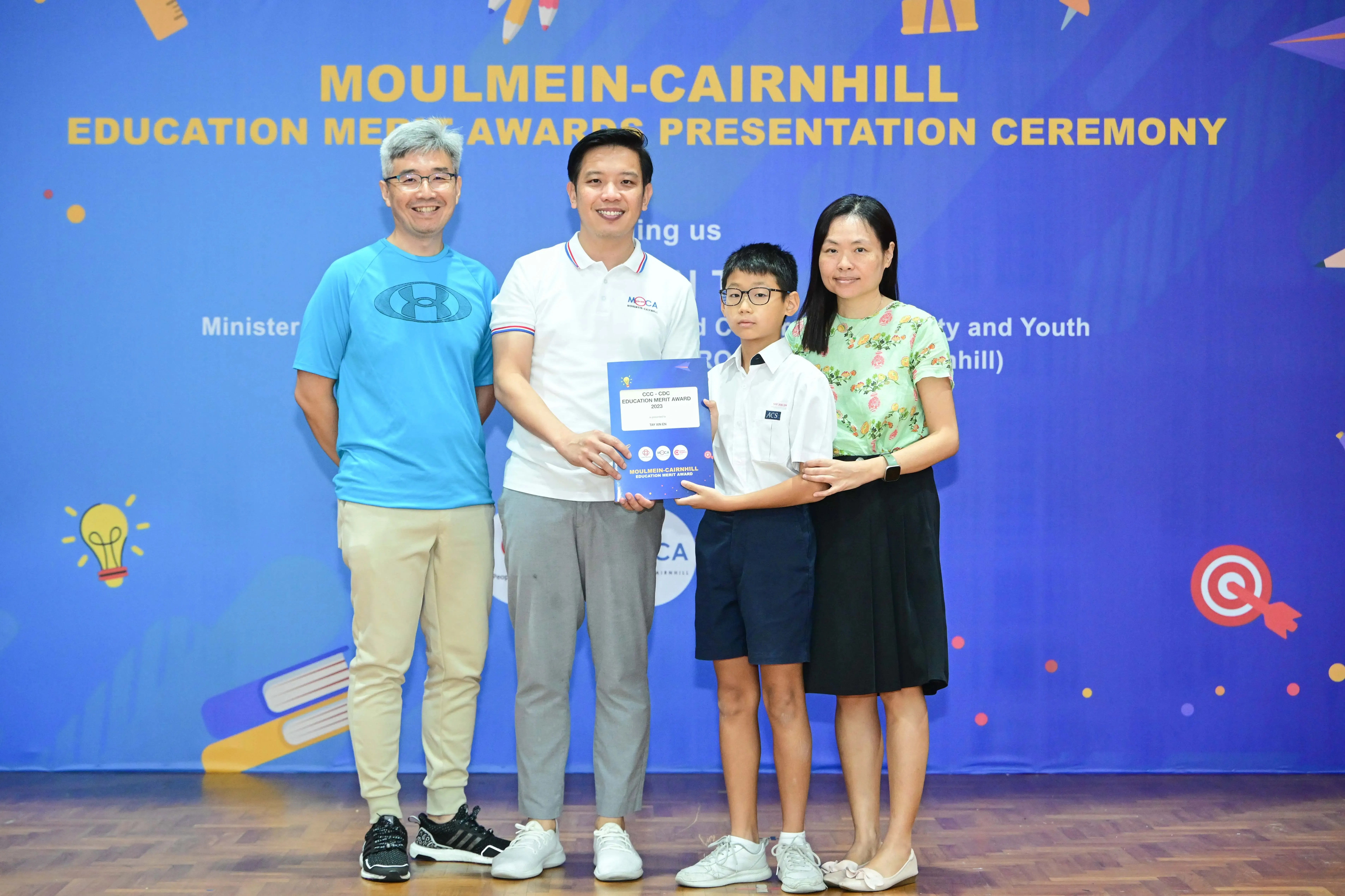 Four people pose holding an award certificate at the Moulmein-Cairnhill Education Merit Awards Presentation Ceremony.
