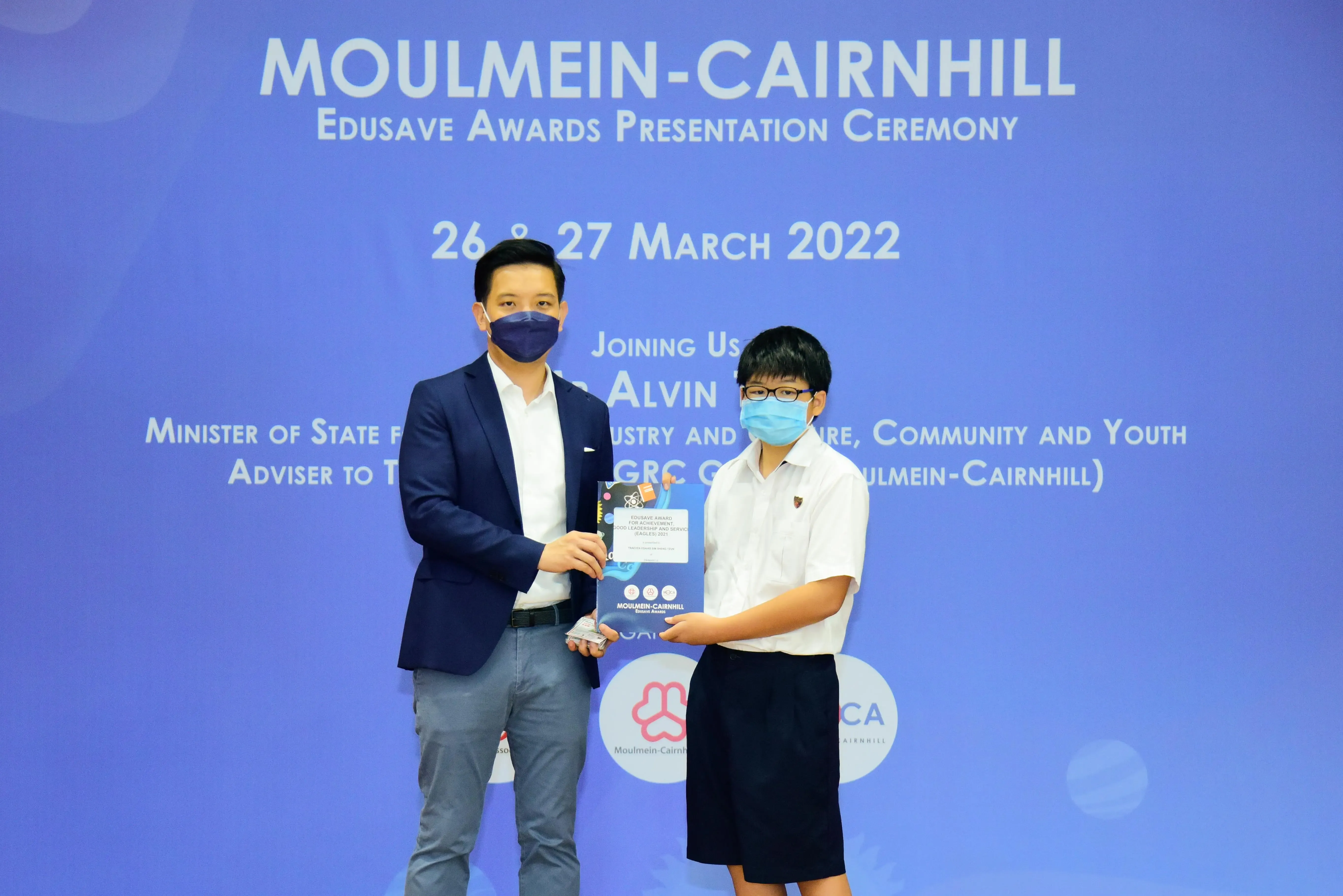 Two masked individuals hold an award together at the Moulmein-Cairnhill Edusave Awards Ceremony, March 2022.