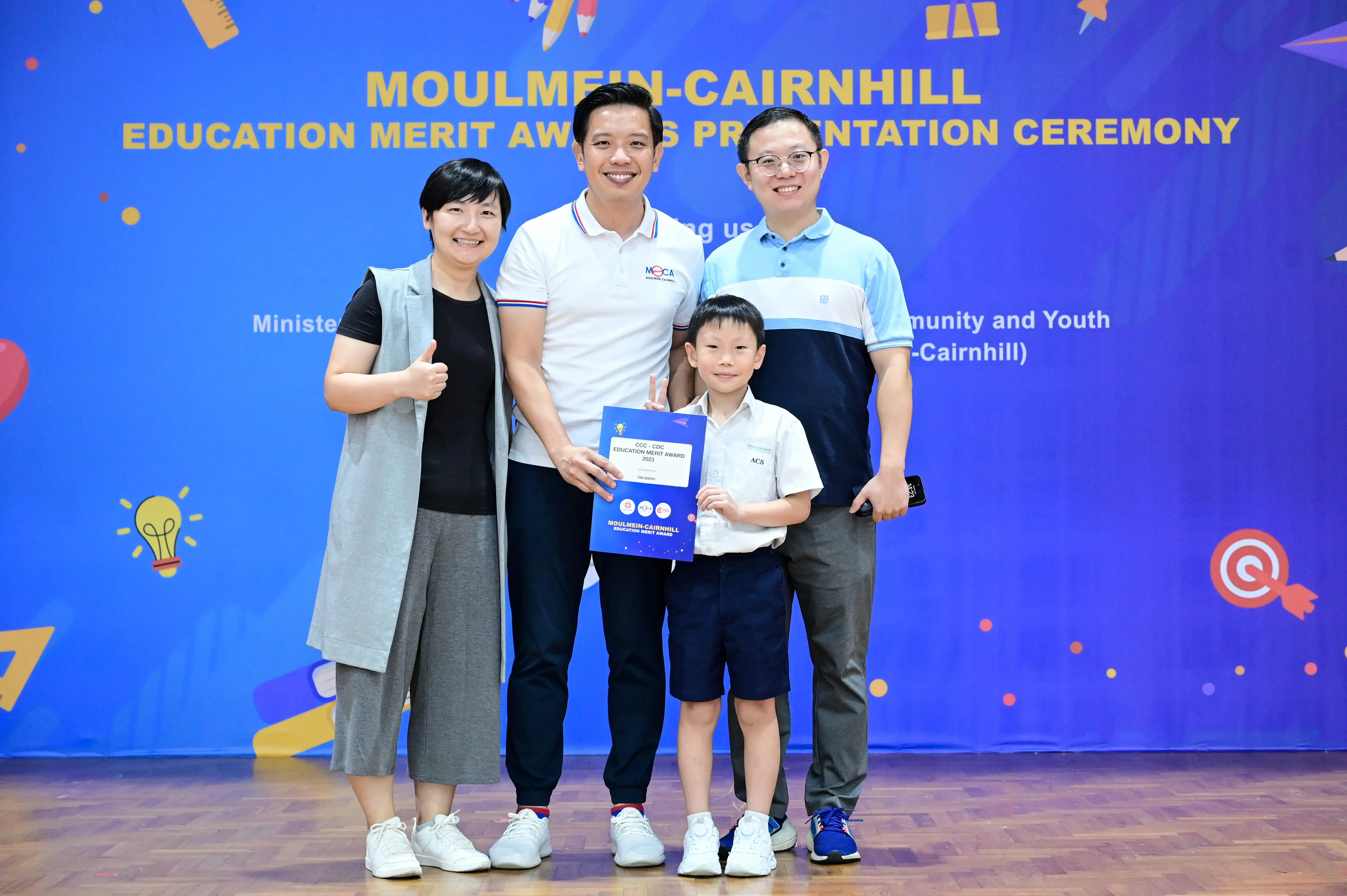 Three adults and a boy holding an award certificate at the Moulmein-Cairnhill Education Merit Awards Presentation Ceremony.