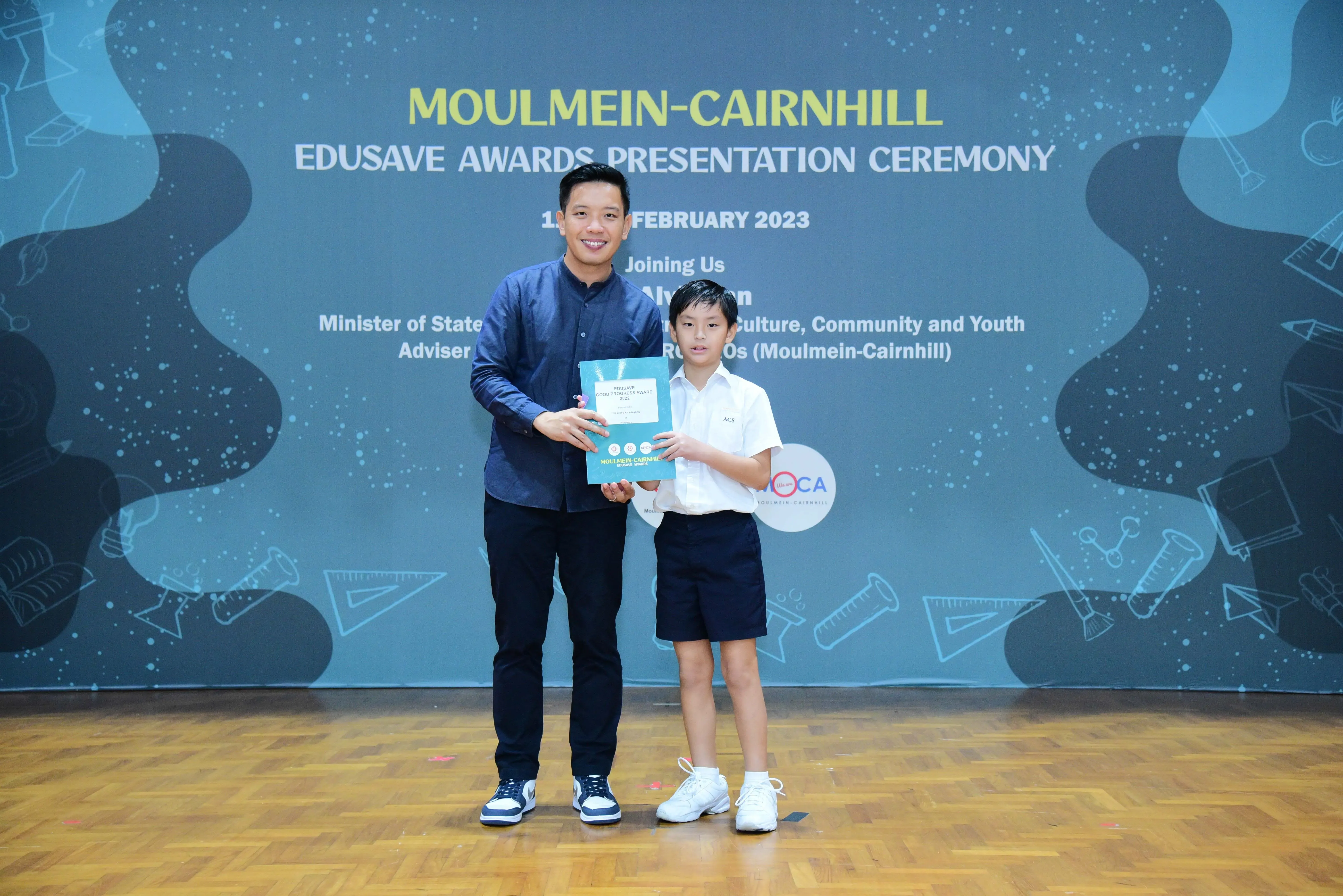An adult and a young student hold an award together at the Moulmein-Cairnhill Edusave Awards Ceremony, February 2023.