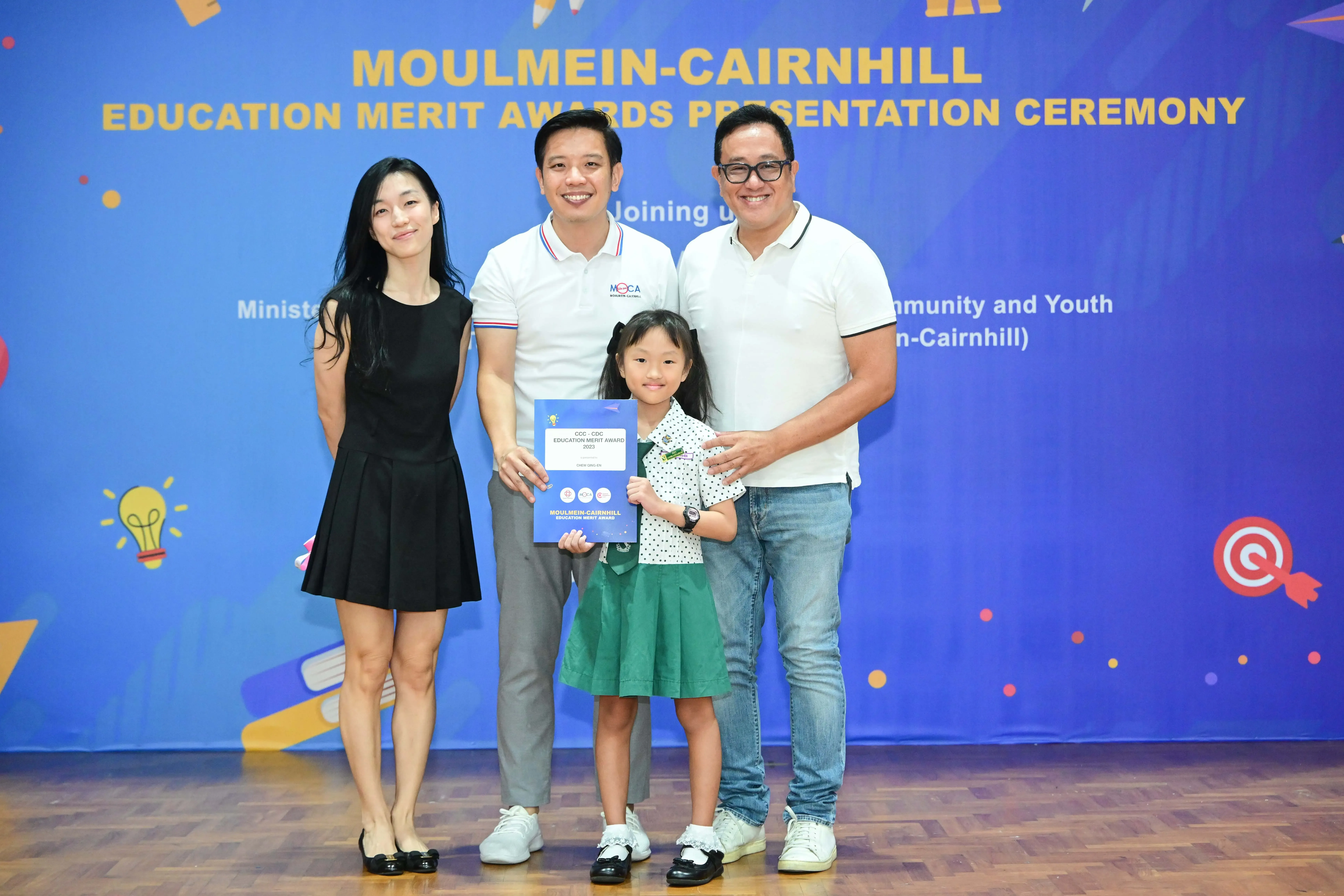 Three adults and a young girl holding an award certificate at the Moulmein-Cairnhill Education Merit Awards ceremony.