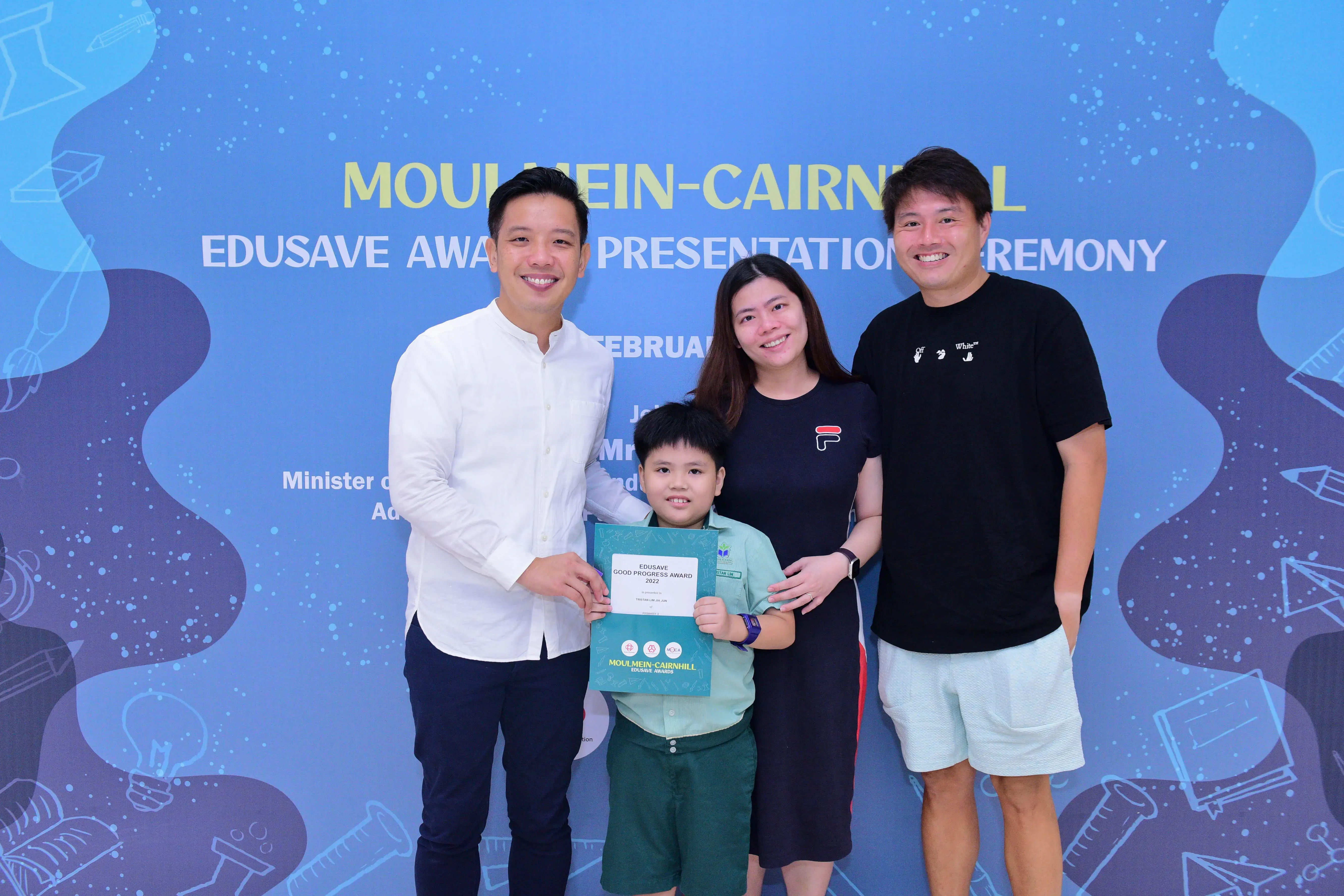 Three adults and a young boy holding an Edusave Good Progress Award certificate at a Moulmein-Cairnhill ceremony.