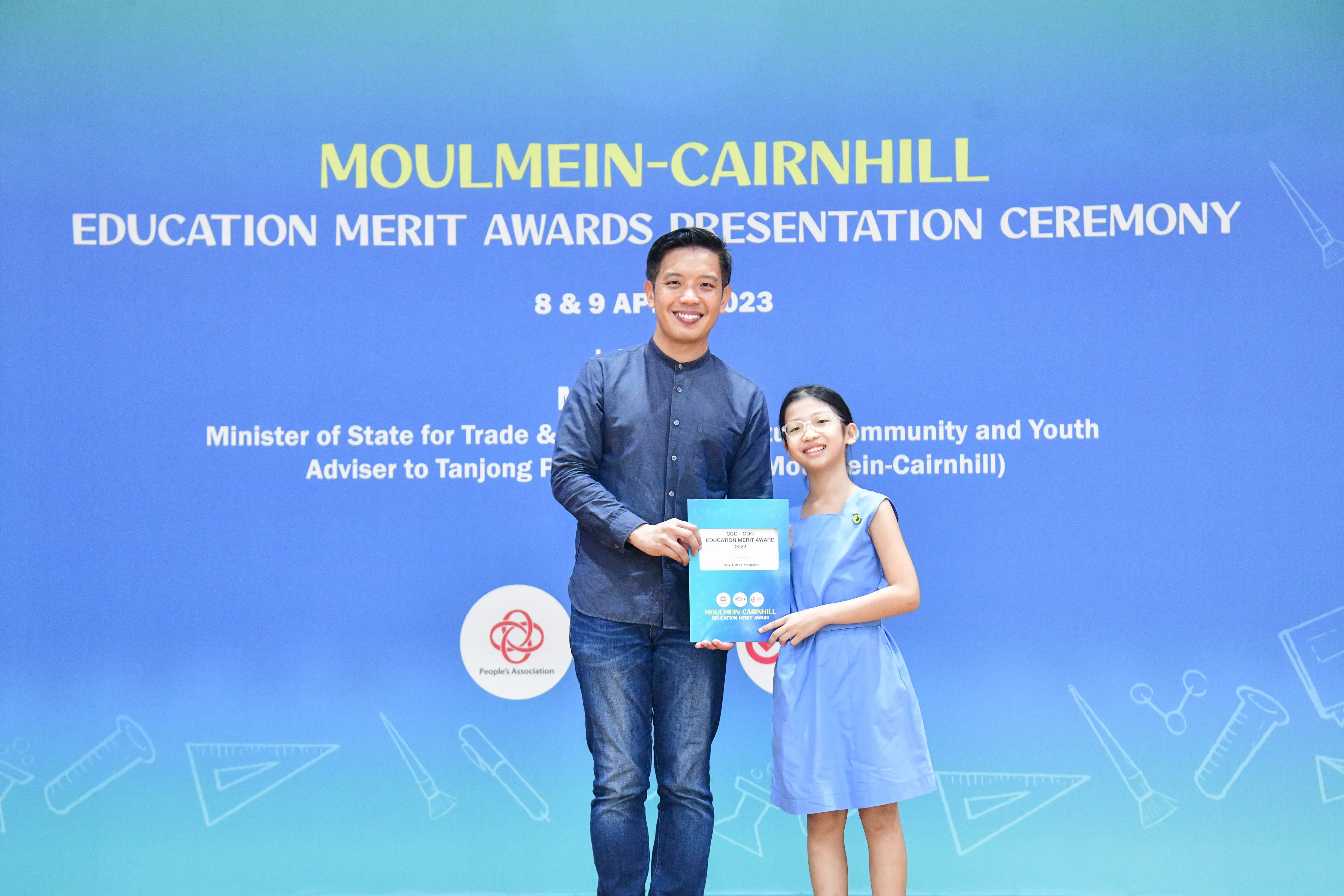 A man and a young girl hold an award certificate at the Moulmein-Cairnhill Education Merit Awards Ceremony, April 2023.