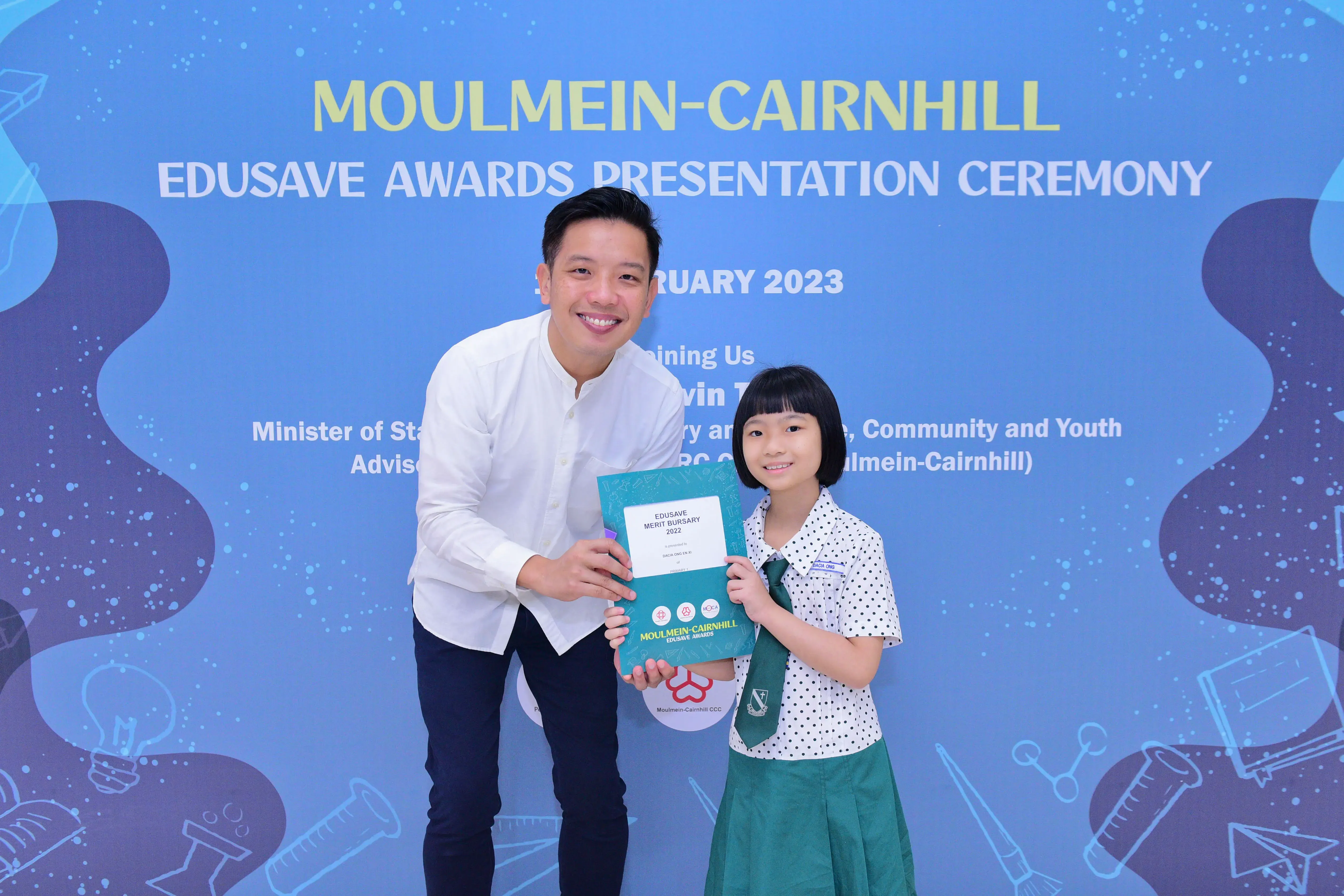 A man and a young girl hold an Edusave Merit Bursary certificate at the Moulmein-Cairnhill Awards Ceremony 2023.