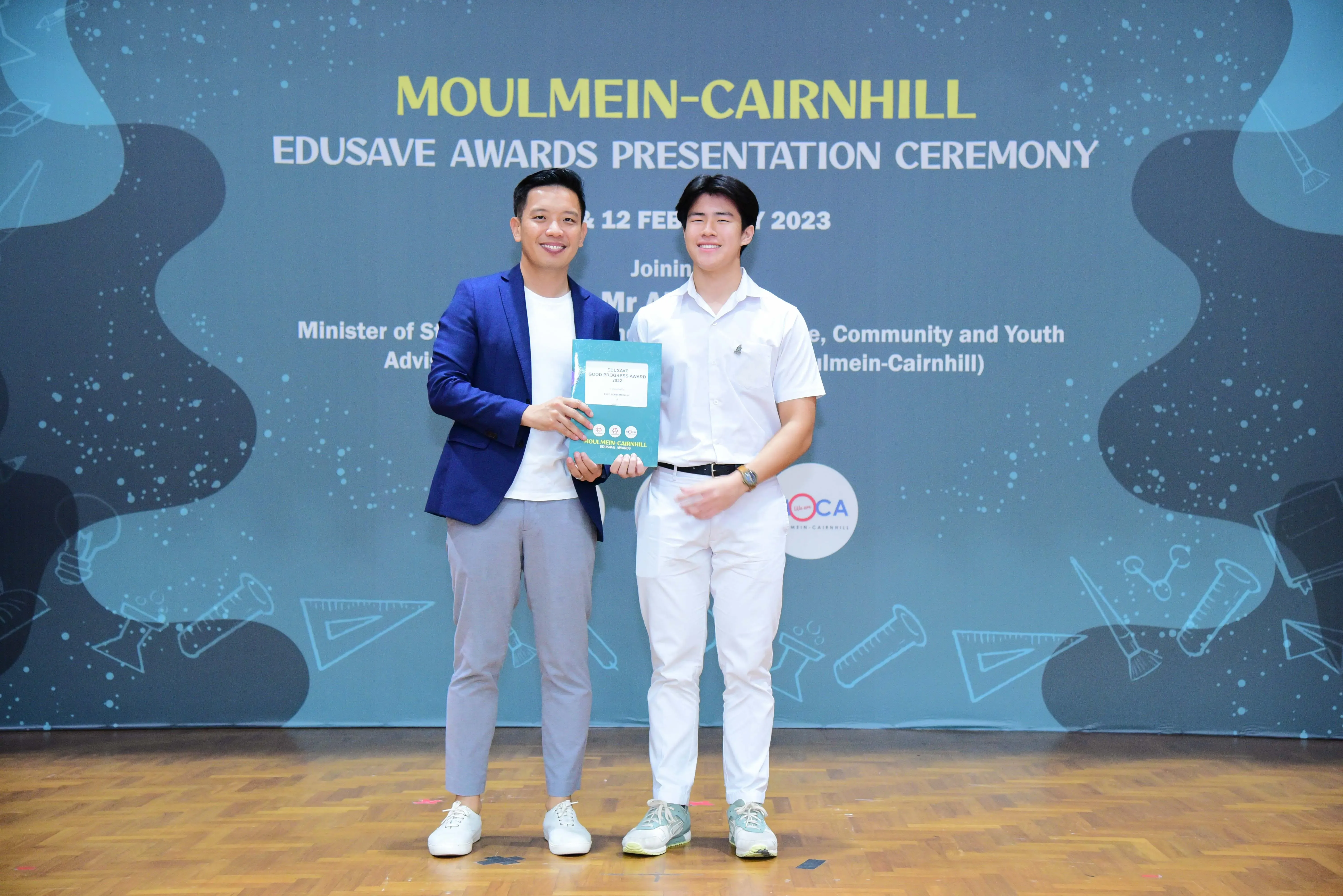 Two men smile holding a certificate at the Moulmein-Cairnhill Edusave Awards Presentation Ceremony 2023.