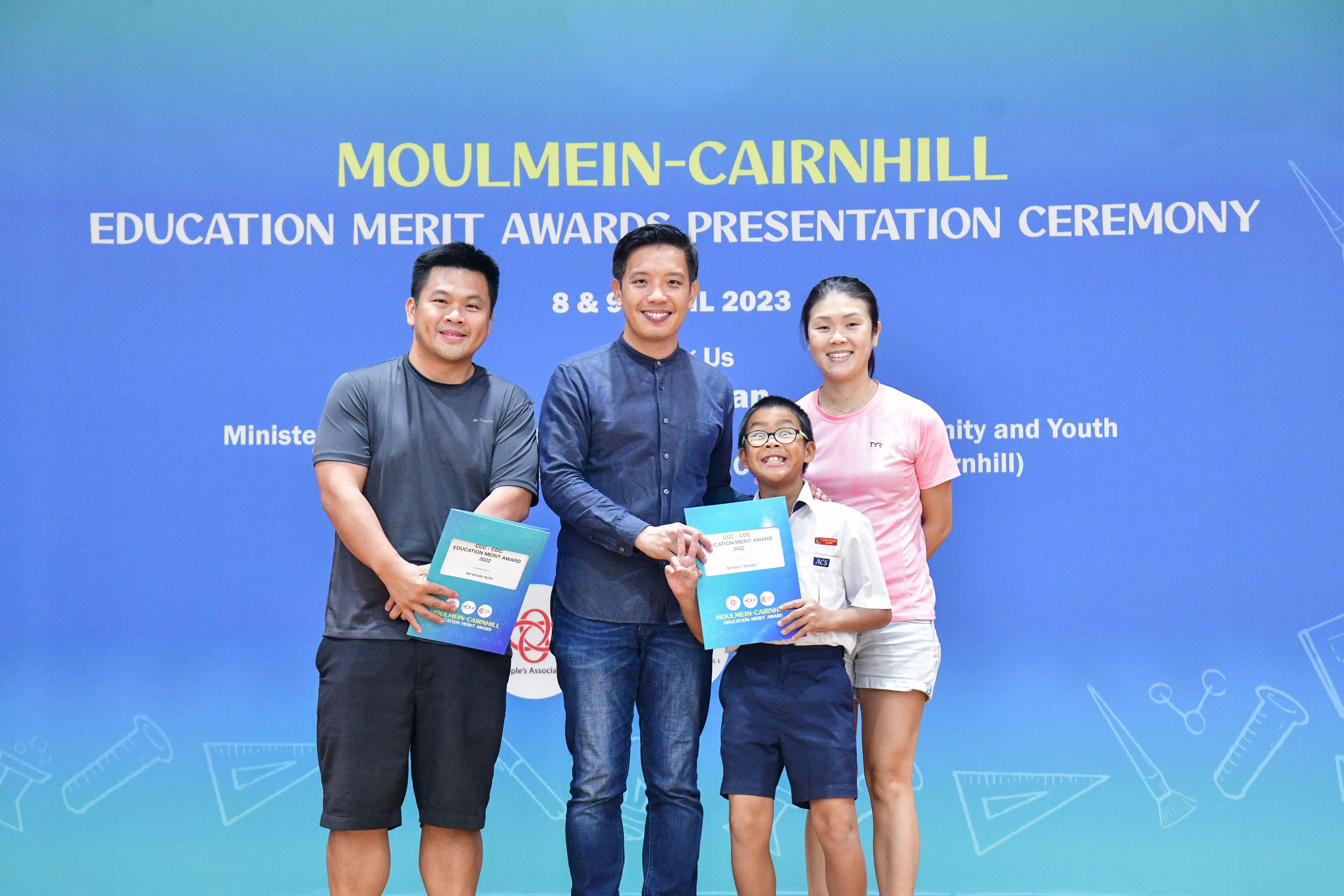 Four people smile holding award folders at the Moulmein-Cairnhill Education Merit Awards Presentation Ceremony 2023.