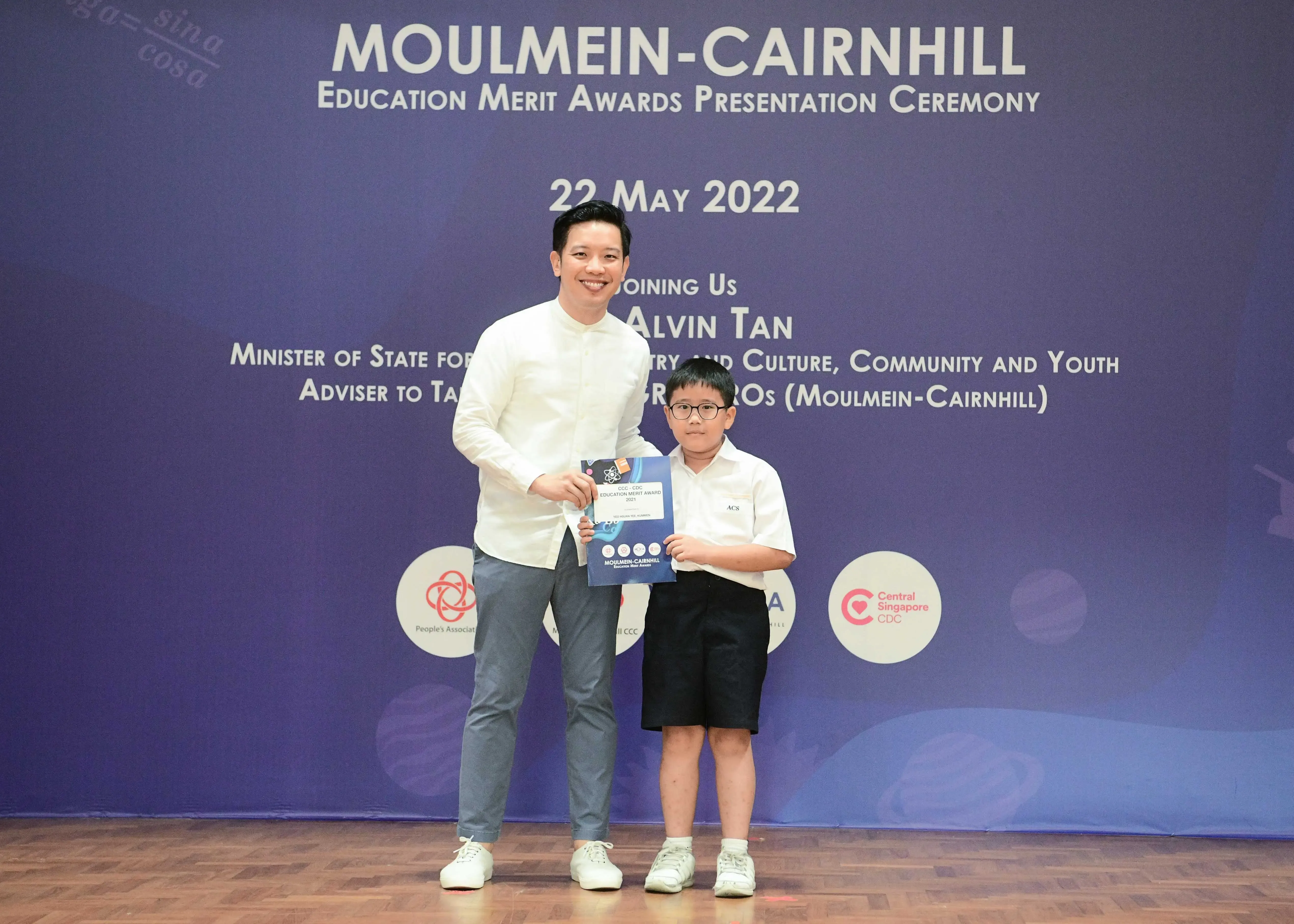 An adult and a young boy hold an award booklet at the Moulmein-Cairnhill Education Merit Awards ceremony on 22 May 2022.